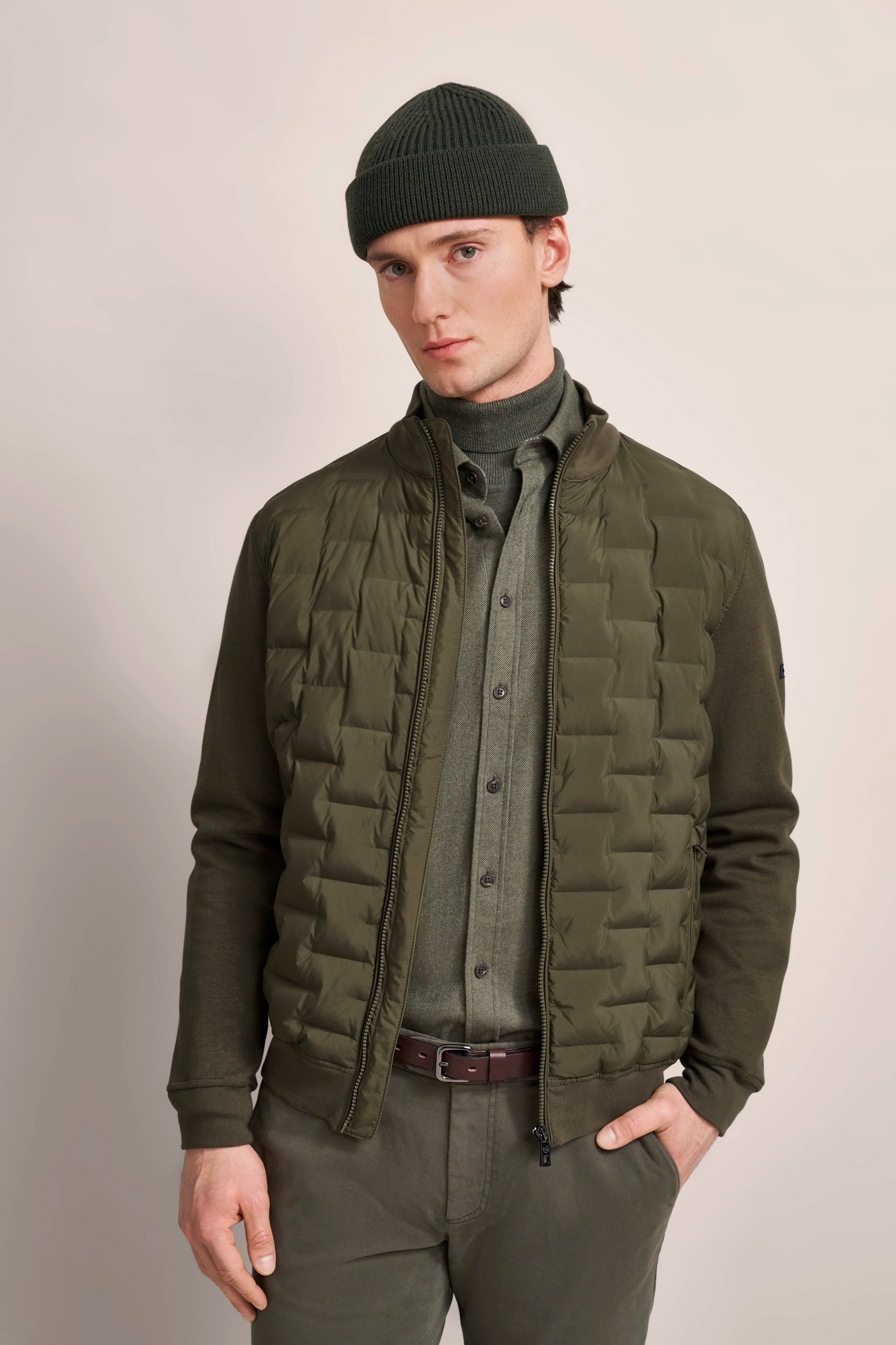 Model in green bugatti outfit with quilted jacket, shirt, and cap, posing casually.