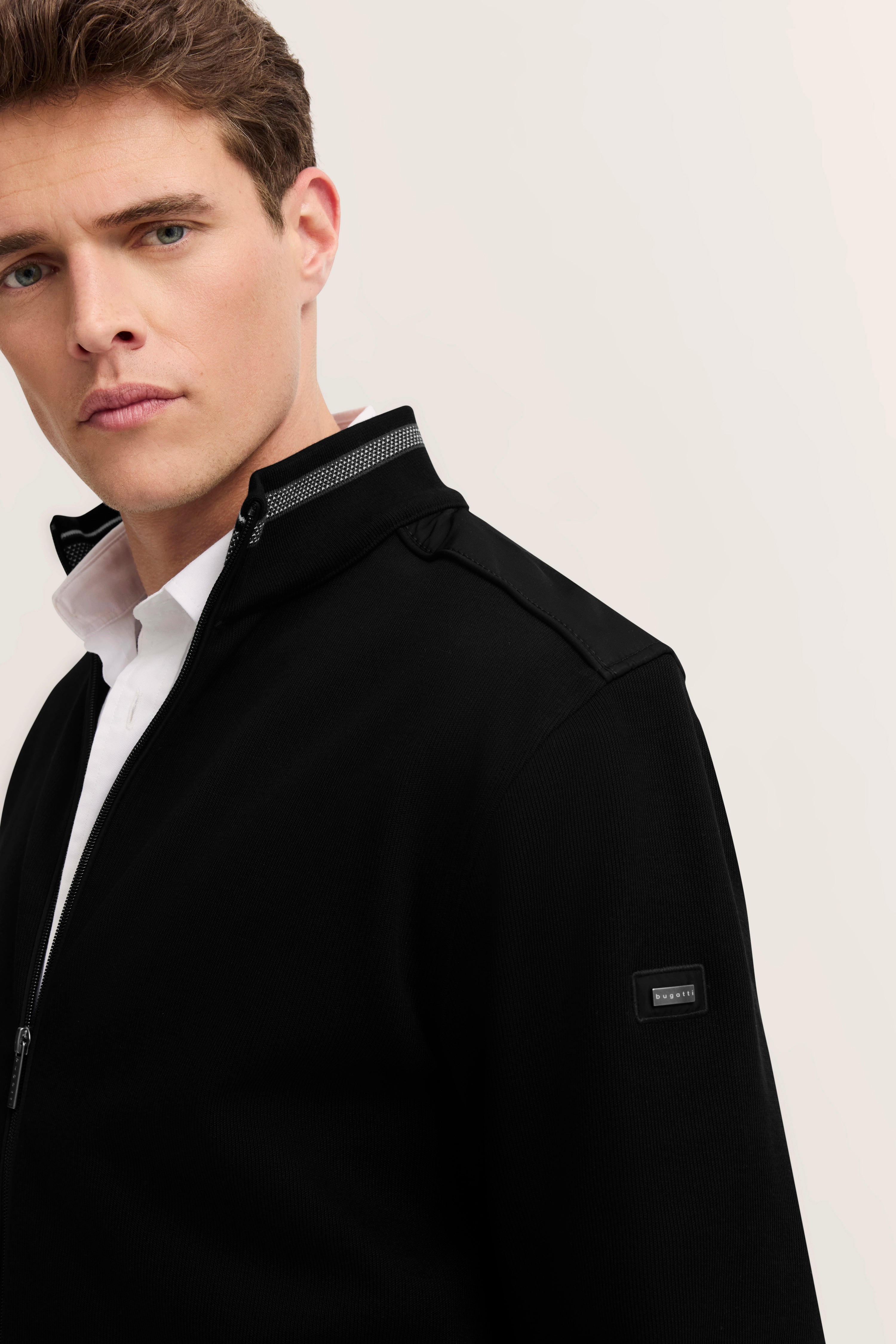 Modelbild, Mann in schwarzer bugatti Jacke mit weißem Hemd, entspanntes Posing.