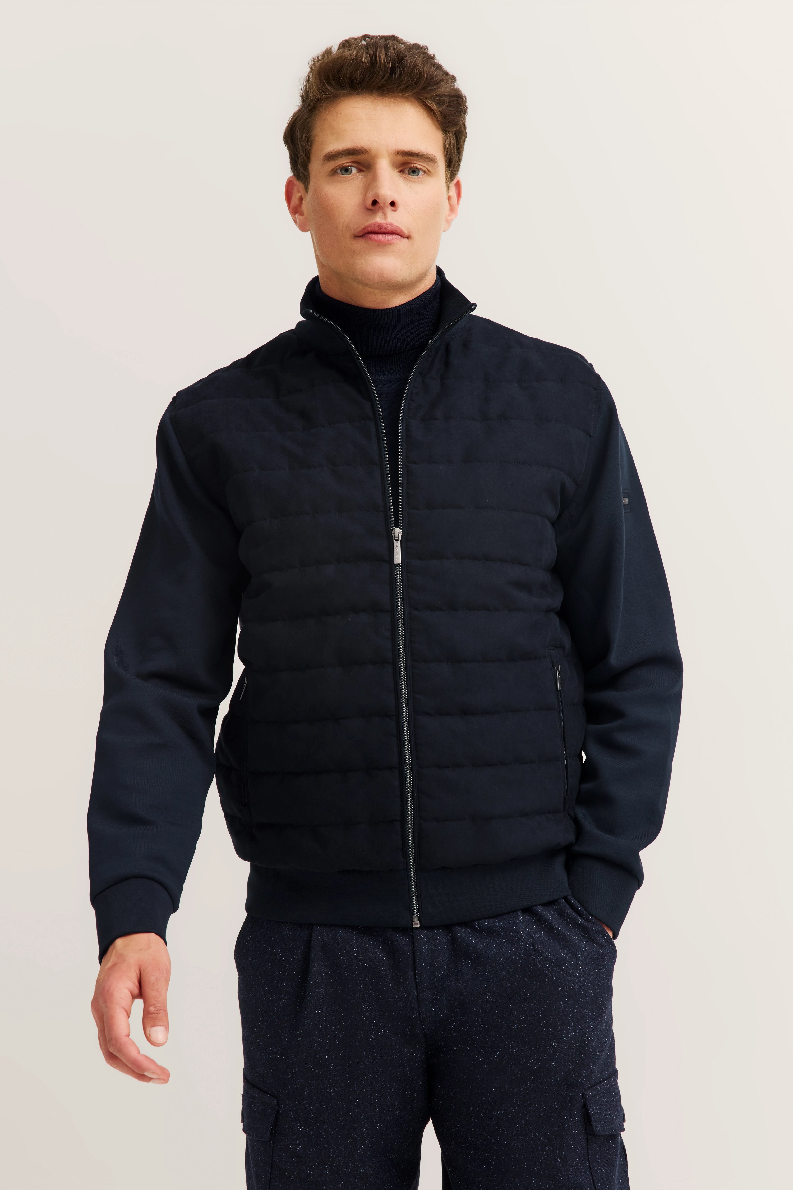 bugatti model in dark blue quilted jacket and turtleneck, standing casually.