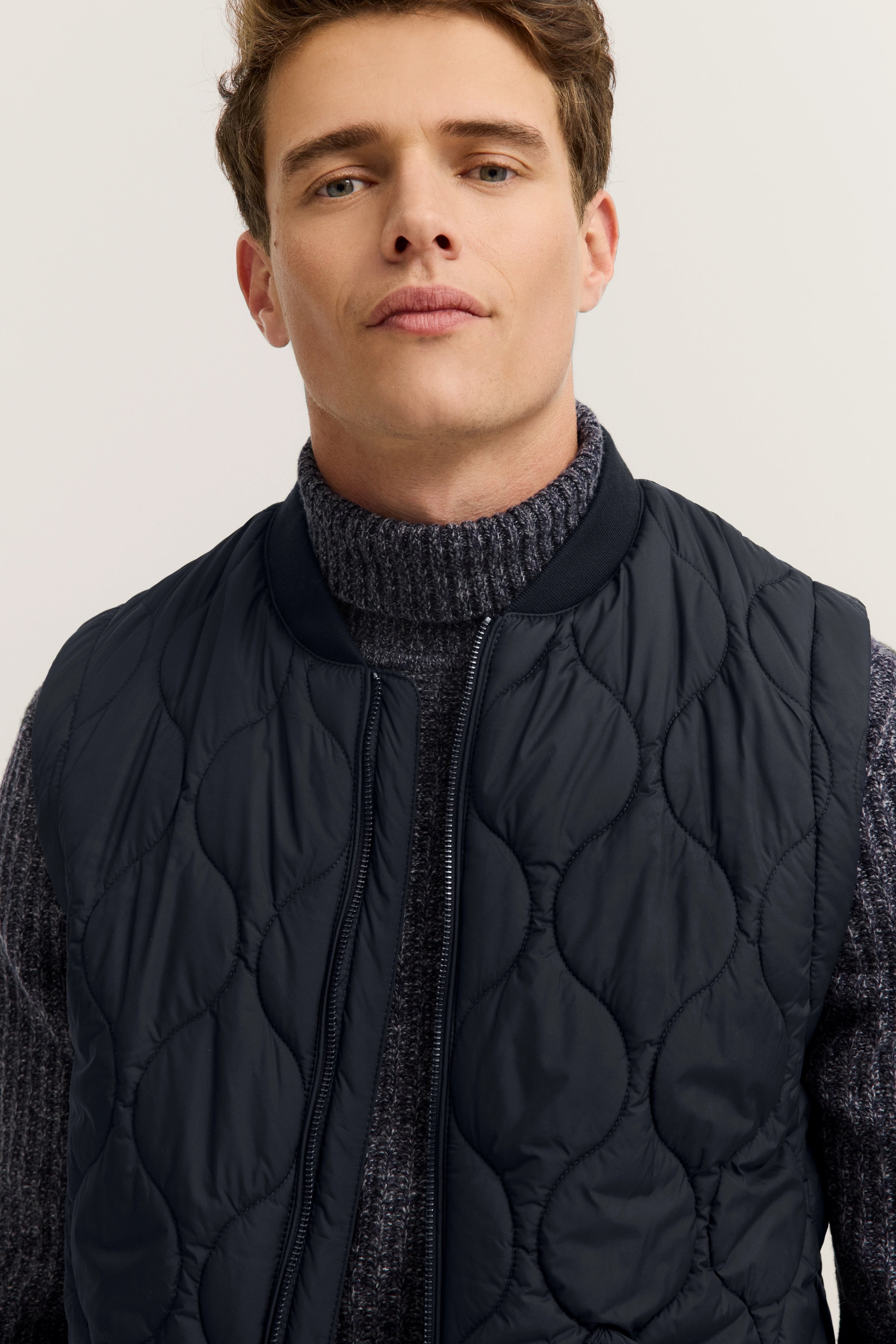 bugatti model in grey turtleneck and quilted dark blue vest, casual pose.