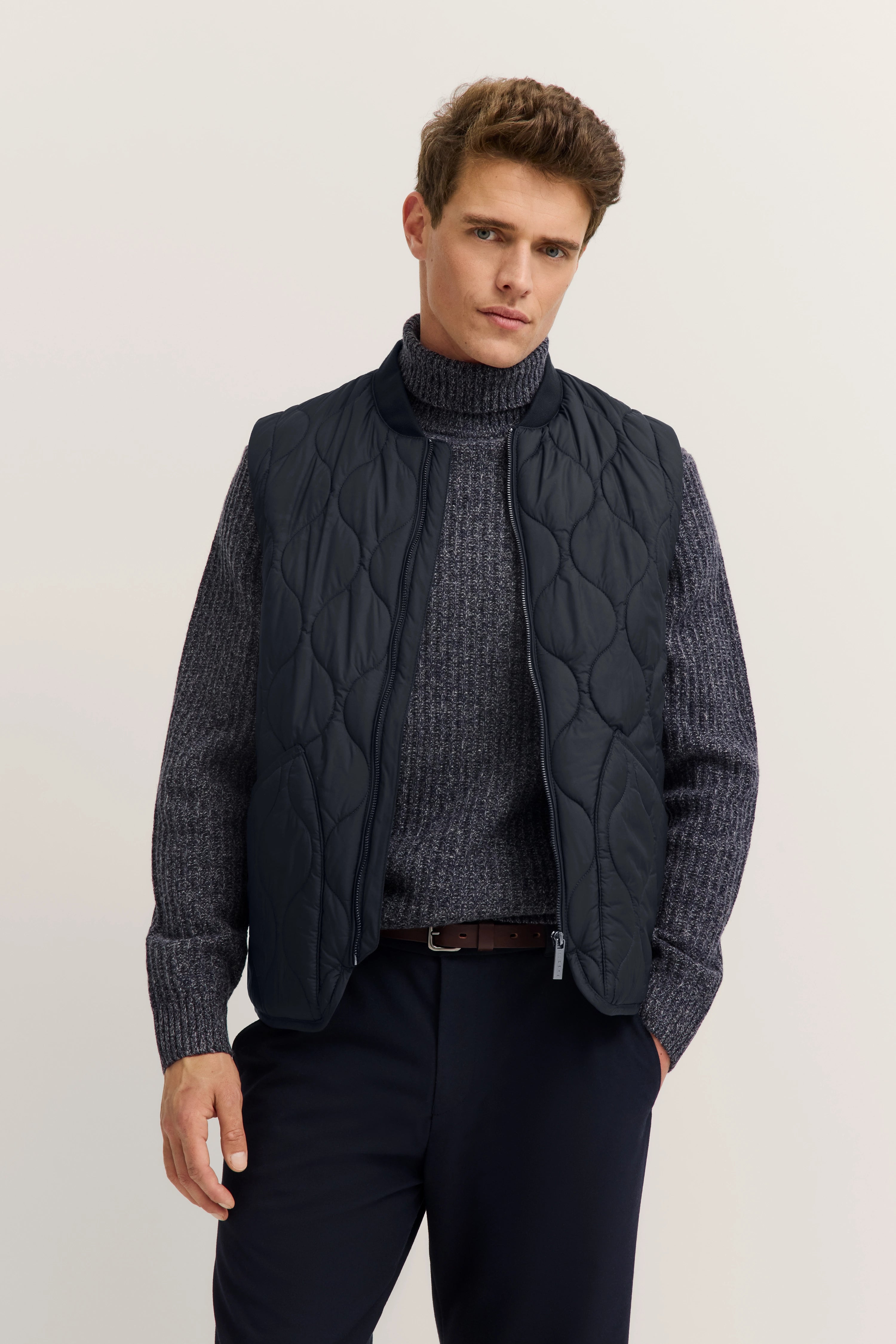 Graumelierter Strickpullover, gesteppte Weste in Dunkelblau, Modelbild, entspannte Pose.