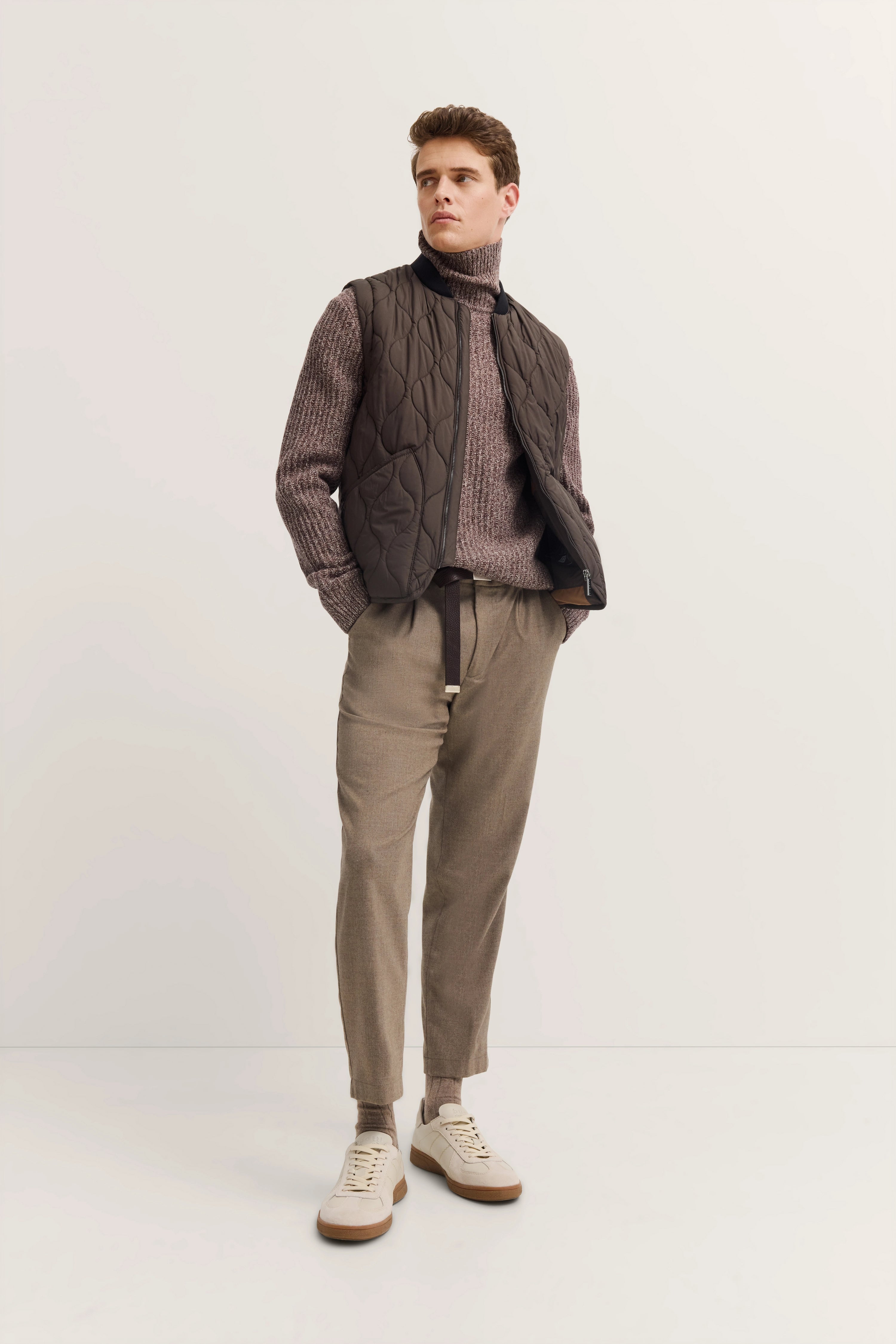 Brown quilted vest over gray knit sweater, beige pants, back view, casual model shot.