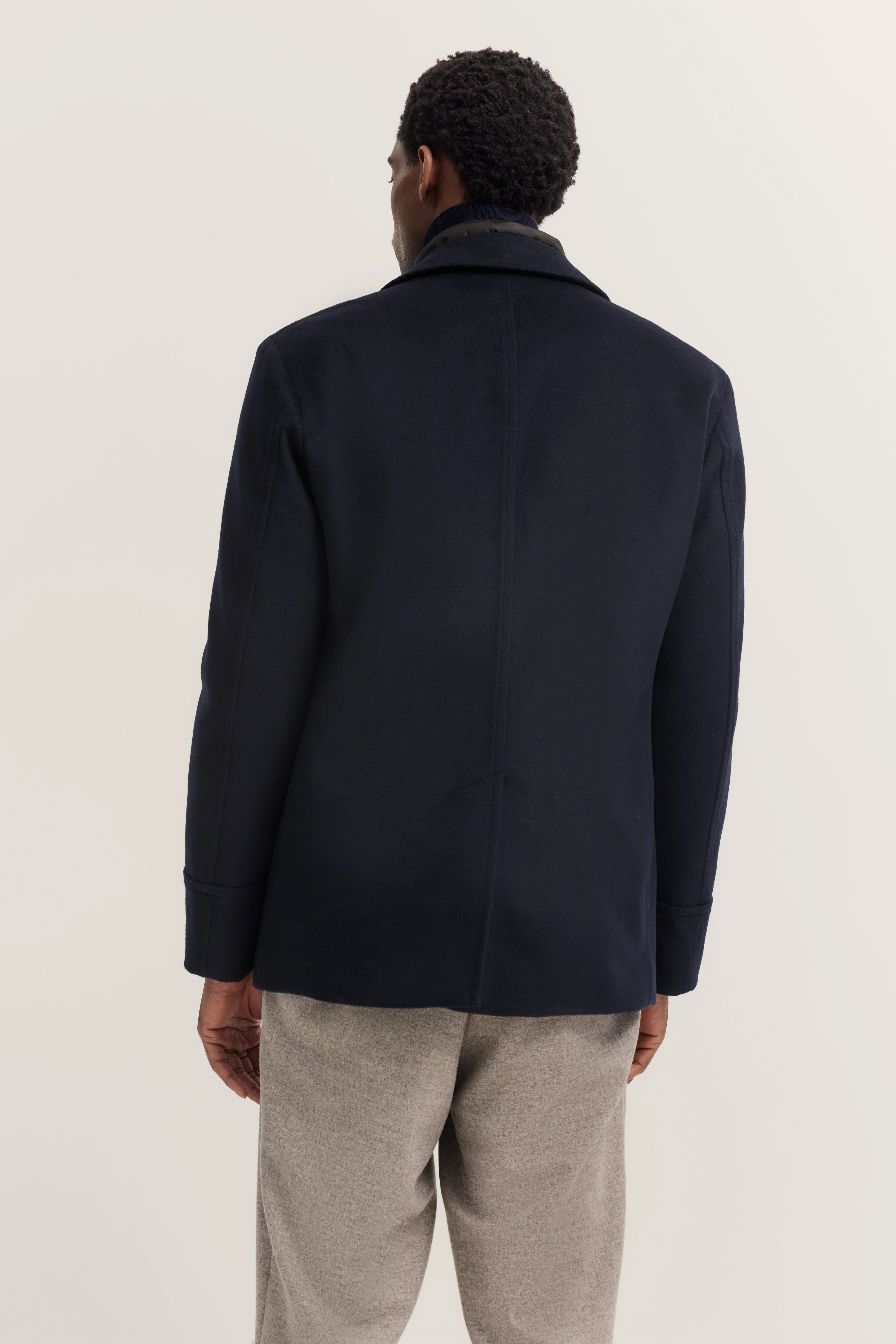 Model in marineblauwe bugatti mantel en grijze broek, achterkant, casual pose.