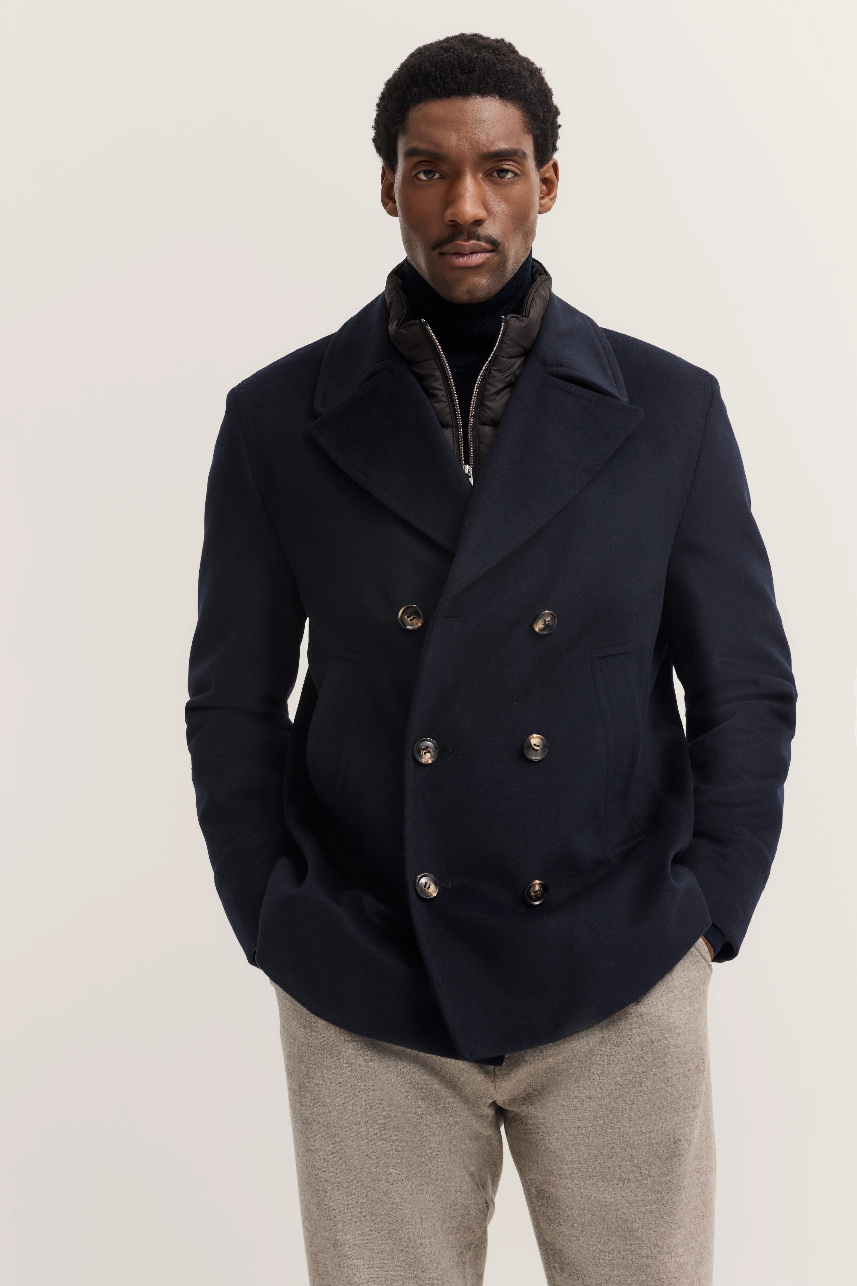 bugatti model in marineblauwe peacoat, grijze broek, ontspannen pose, stijlvol en elegant.