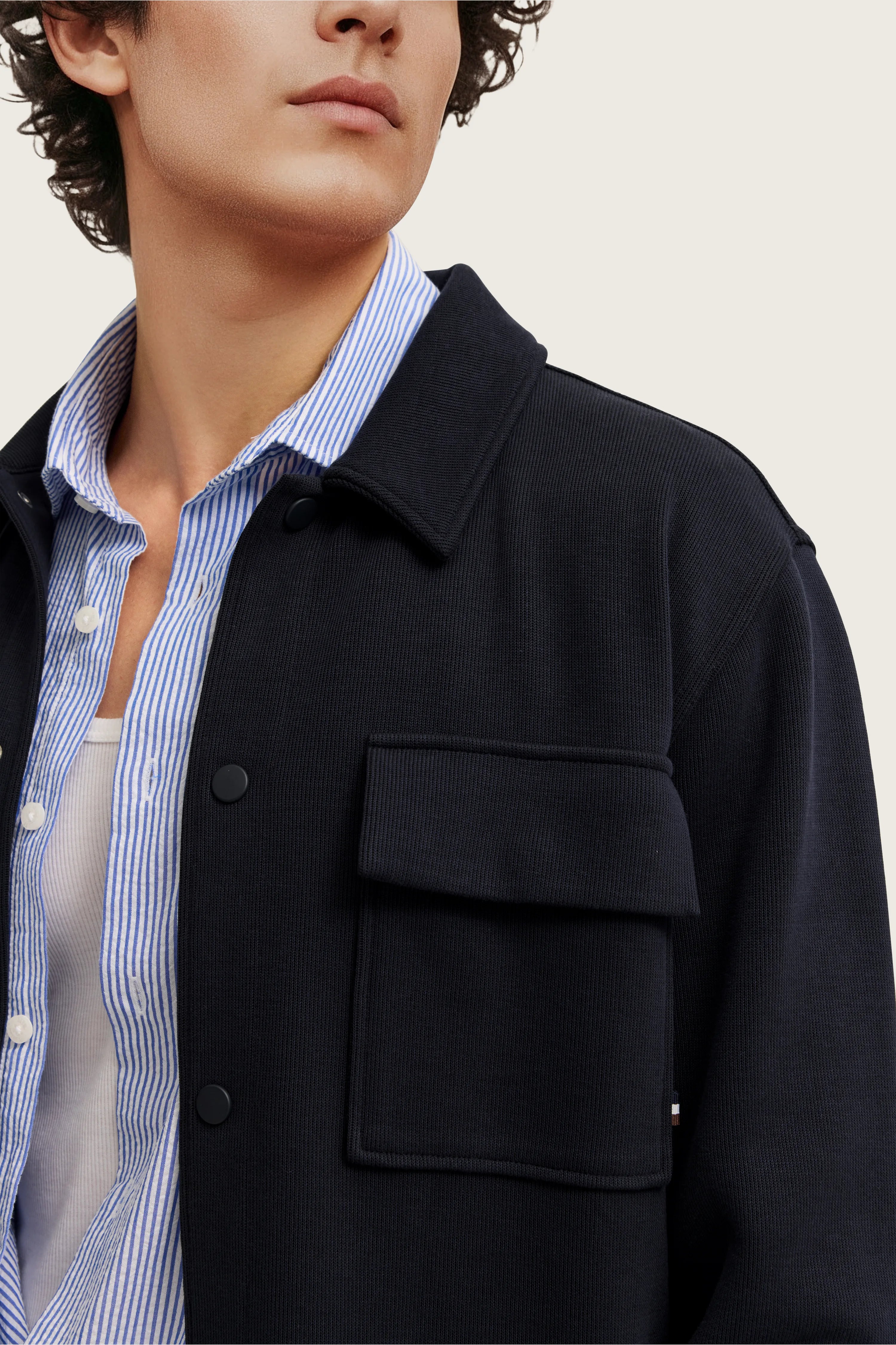 Büstenbild mit dunkelblauer Jacke über blau-weiß gestreiftem Hemd, legerer Stil.