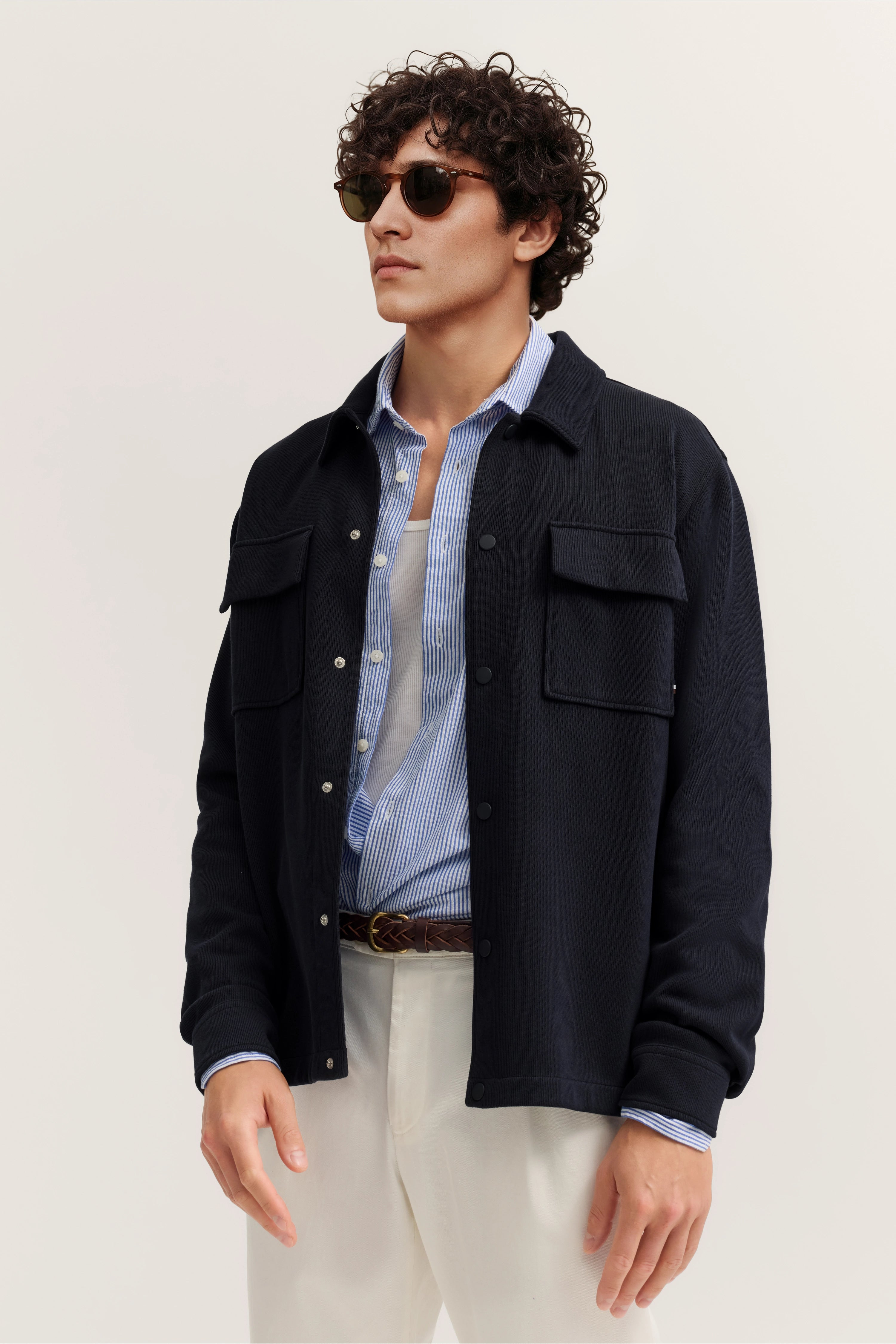 Model in dunkelblauer Jacke, gestreiftem Hemd, weißem T-Shirt und beiger Hose, bugatti Stil.