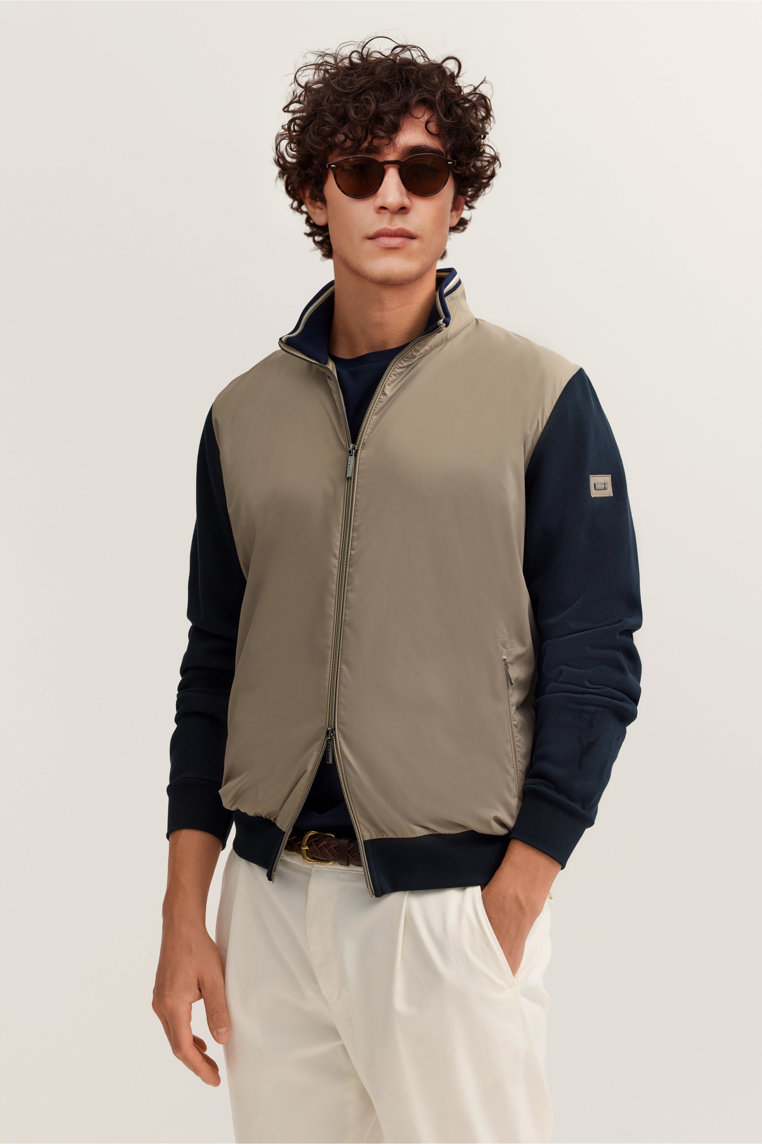 Herrenmodel in beige Weste mit dunkelblauen Ärmeln, weißer Hose