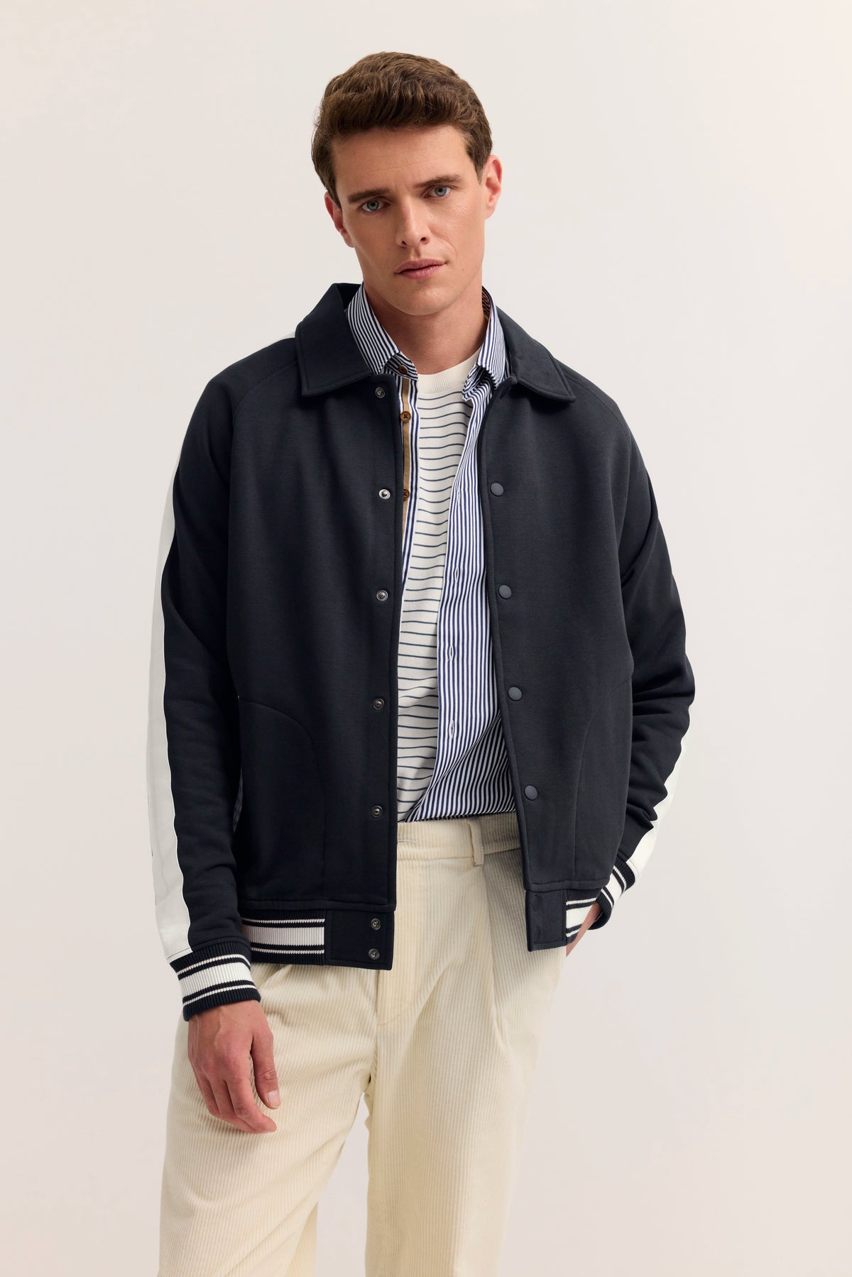Modelbild: Mann trägt schwarze Jacke, gestreiftes Hemd, cremefarbene Hose