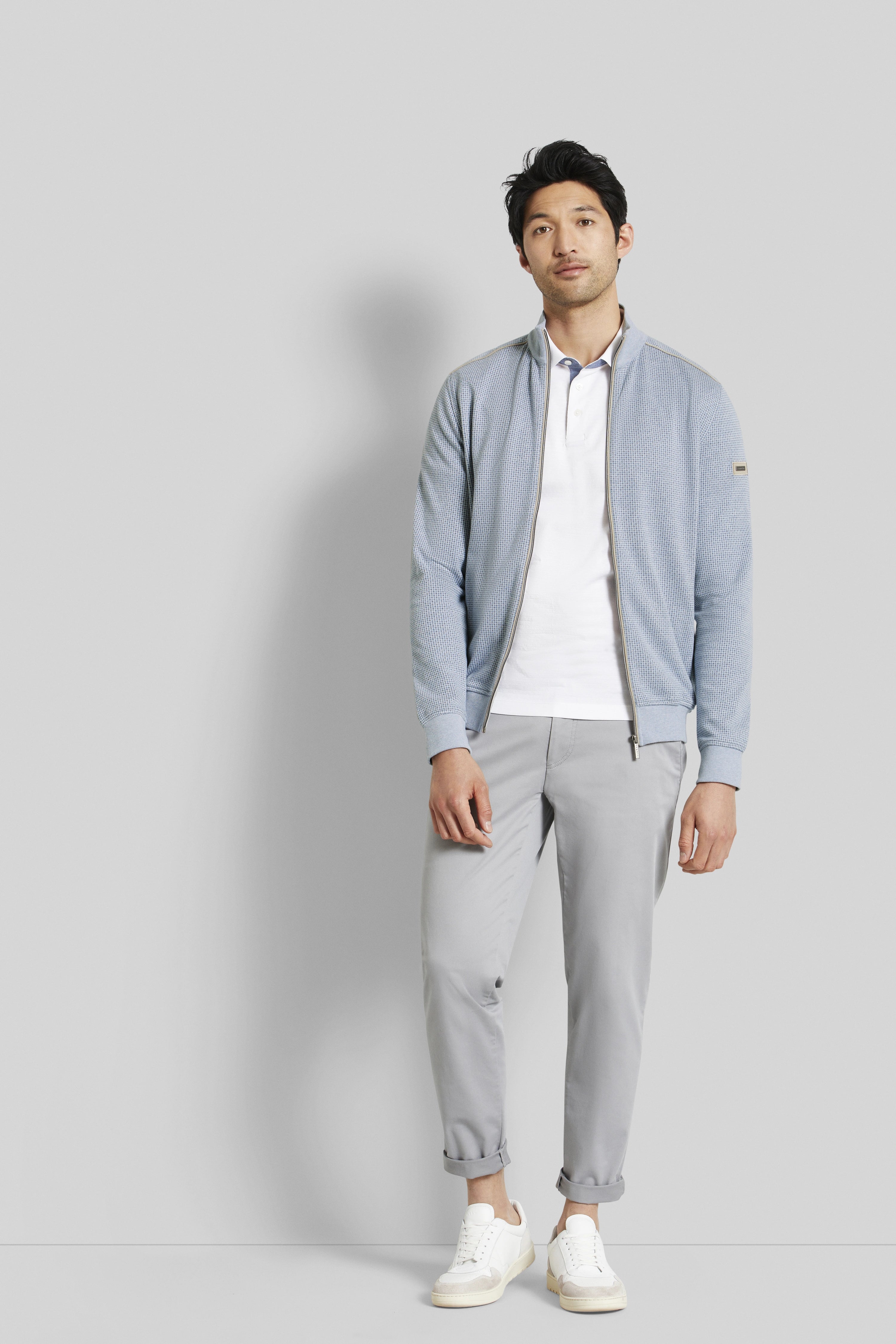 bugatti model in light blue jacket, white polo, gray pants, white sneakers, casual stance.