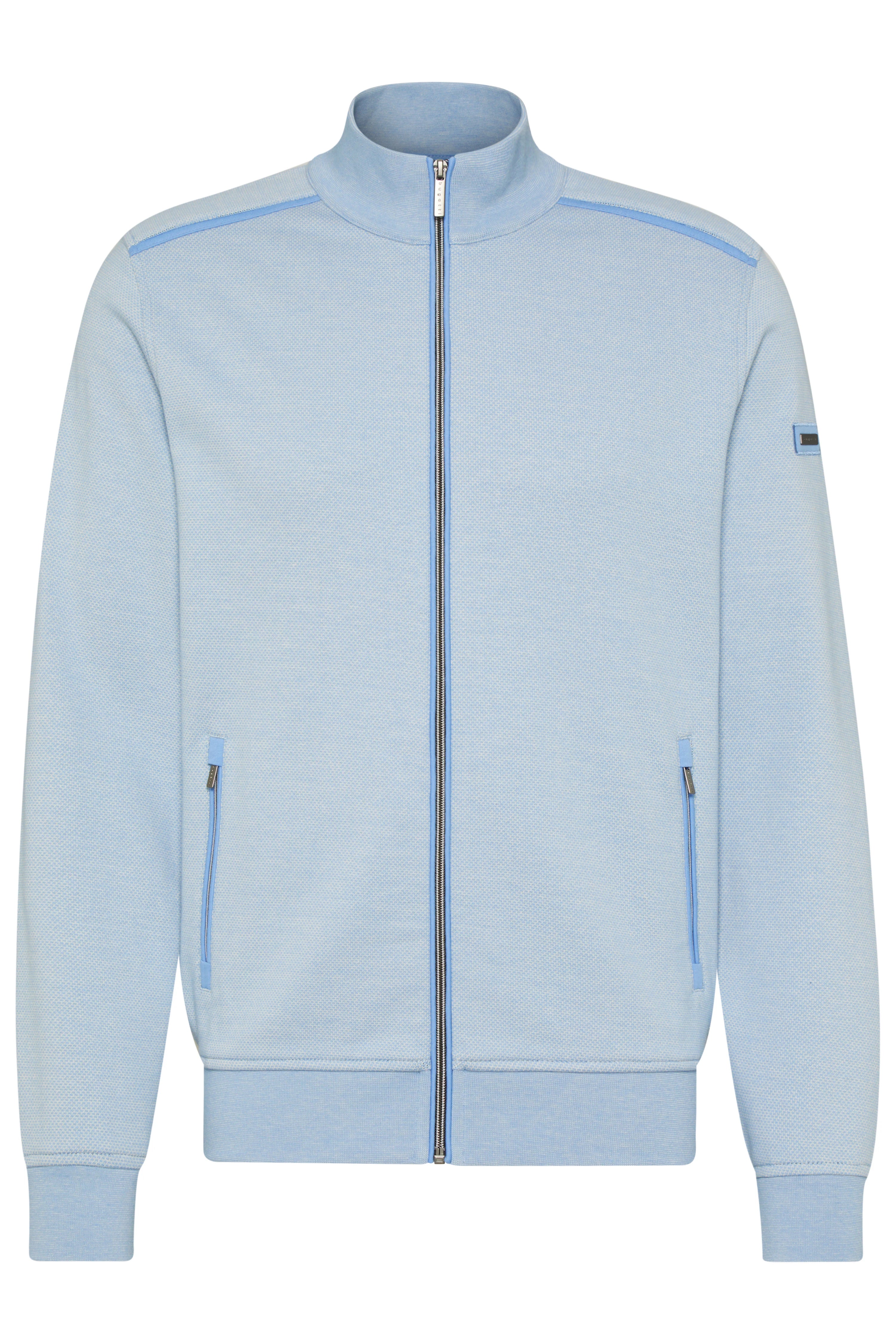 Model in light blue sweater, dark pants, casual pose, seen from the back.