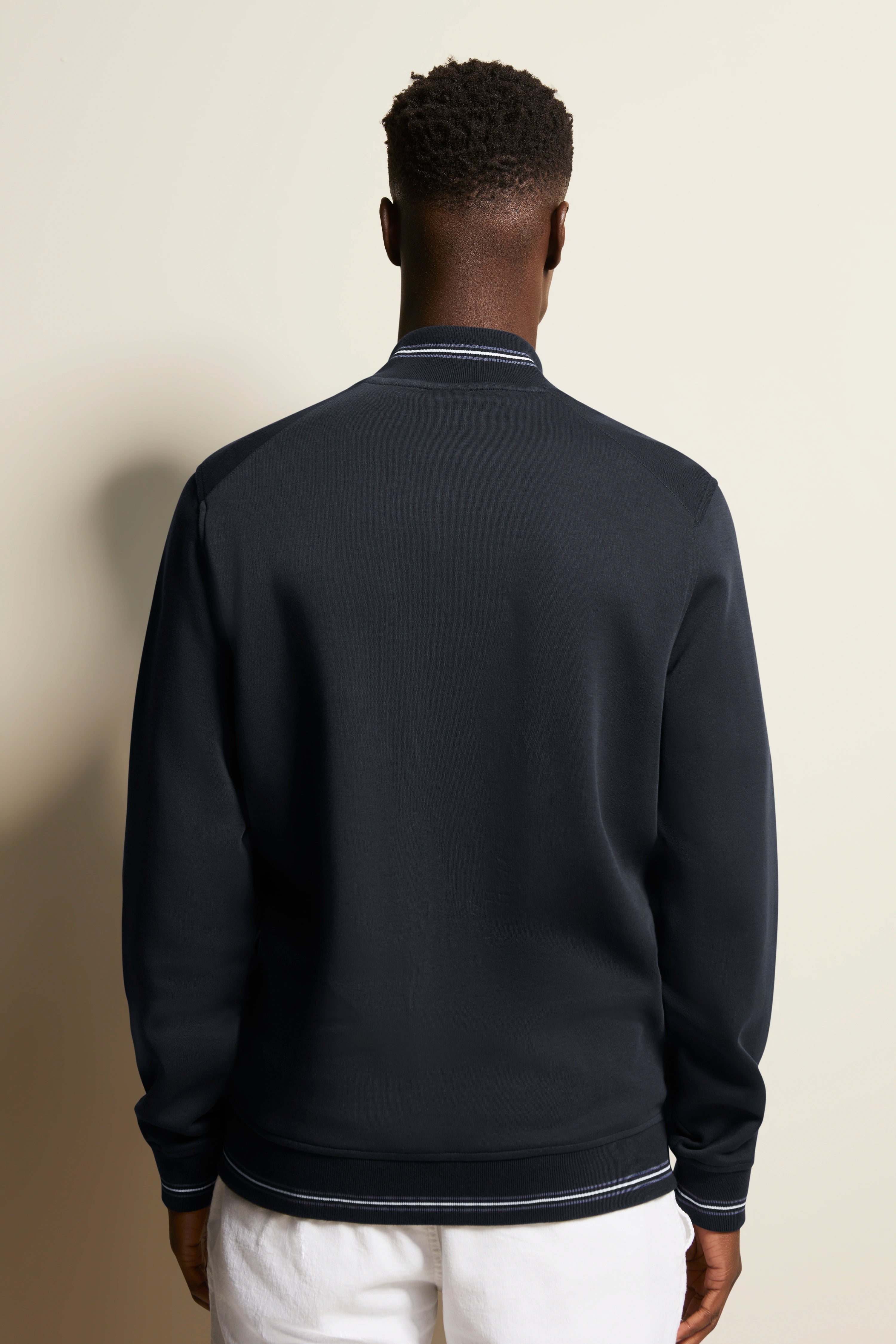 Back view of model in navy bugatti sweatshirt, white pants, casual style, relaxed pose.