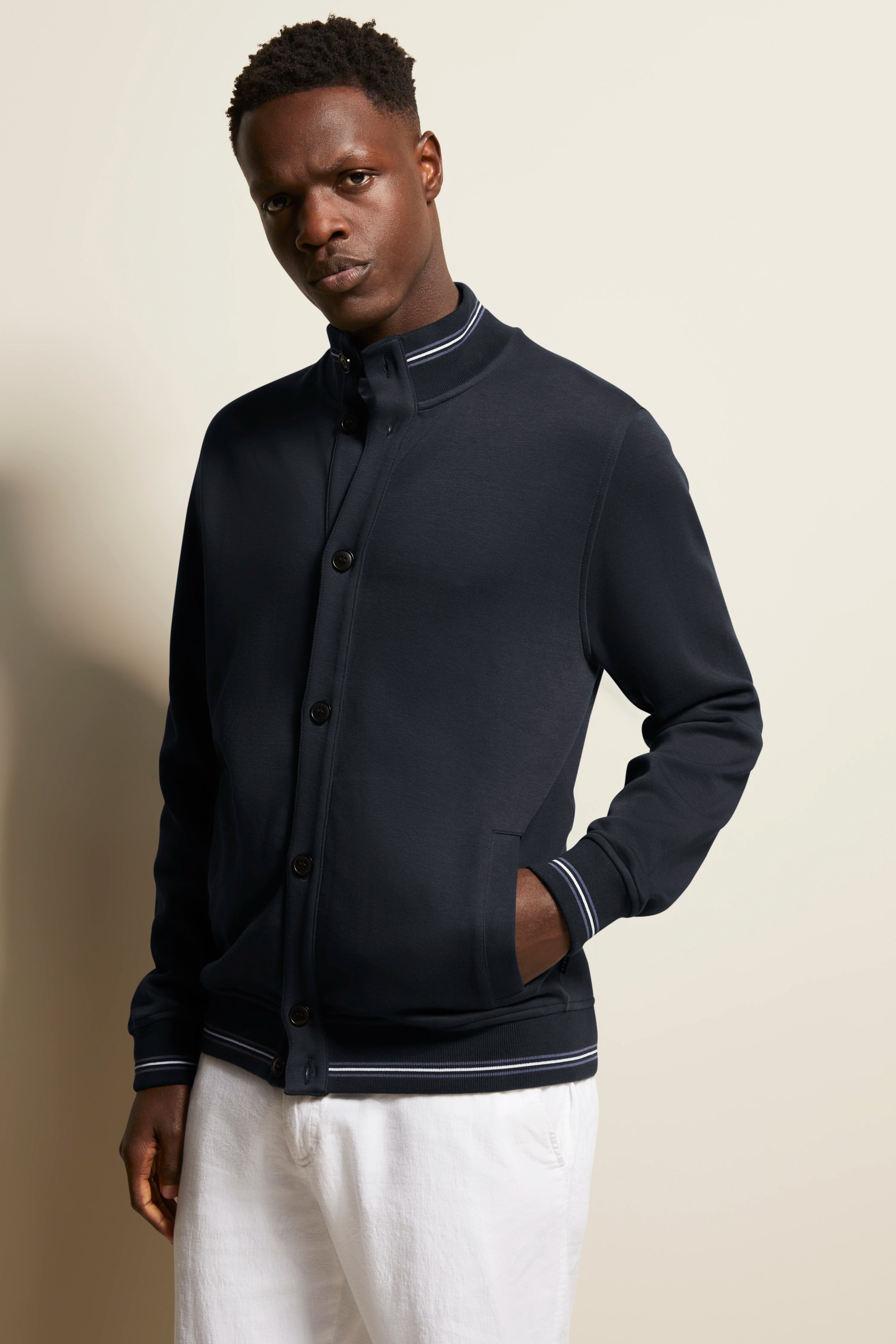 Model in navy bugatti jacket with white stripes, white pants, casual pose.