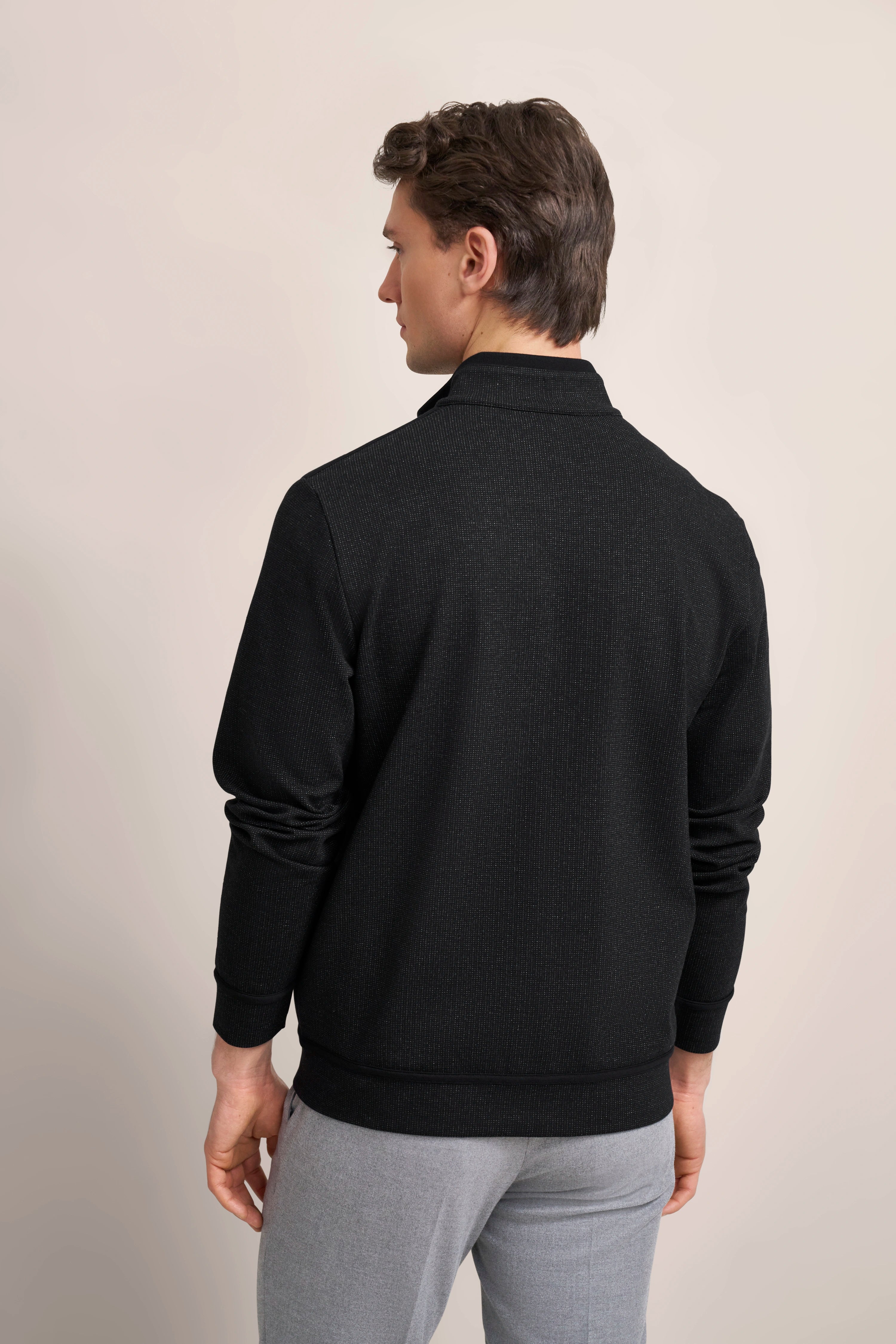 Model in schwarzem bugatti Pullover mit grauer Hose, Rückenansicht, entspannte Pose.
