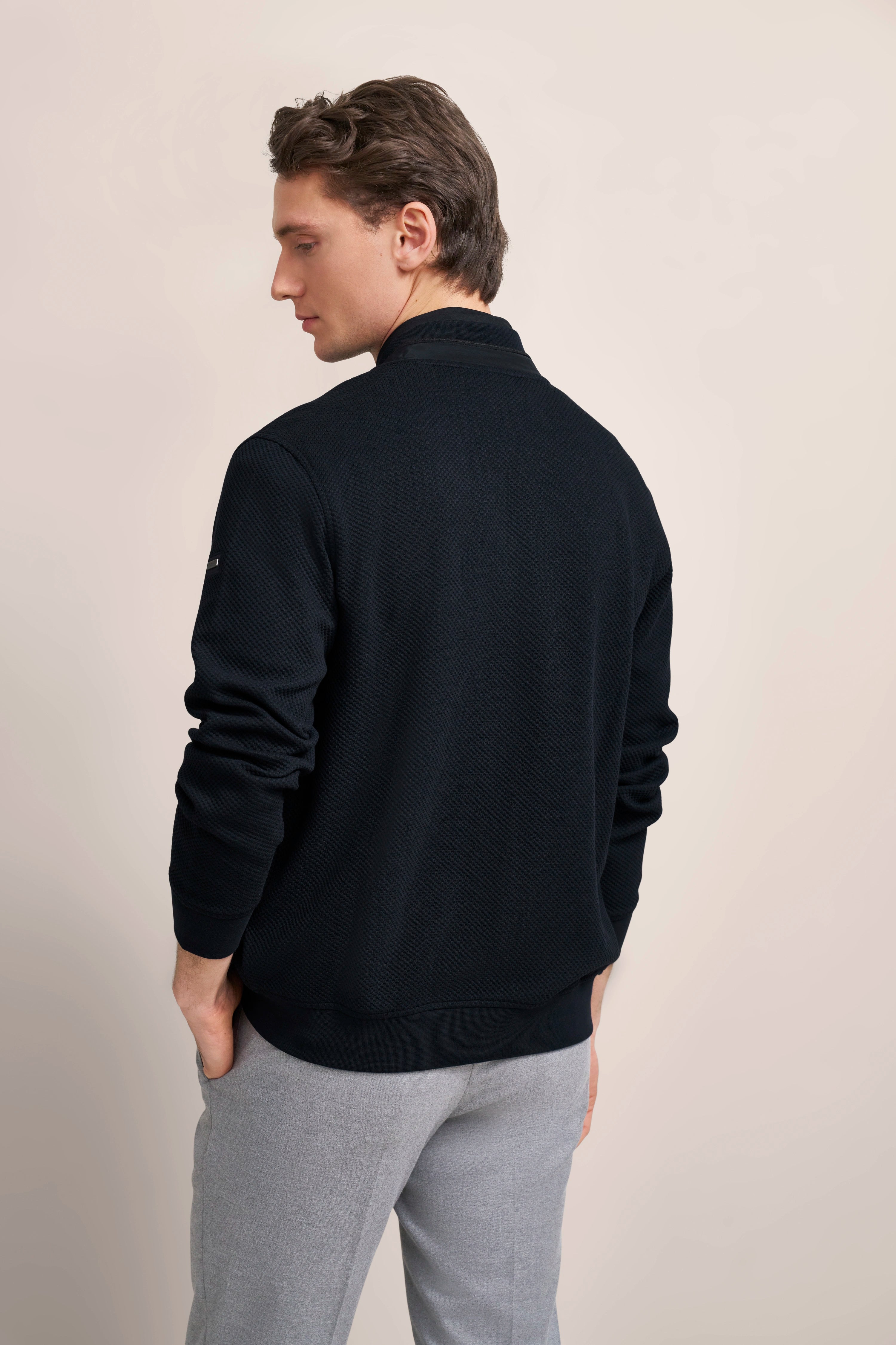 Model in black bugatti sweater and gray pants, side view, relaxed pose.