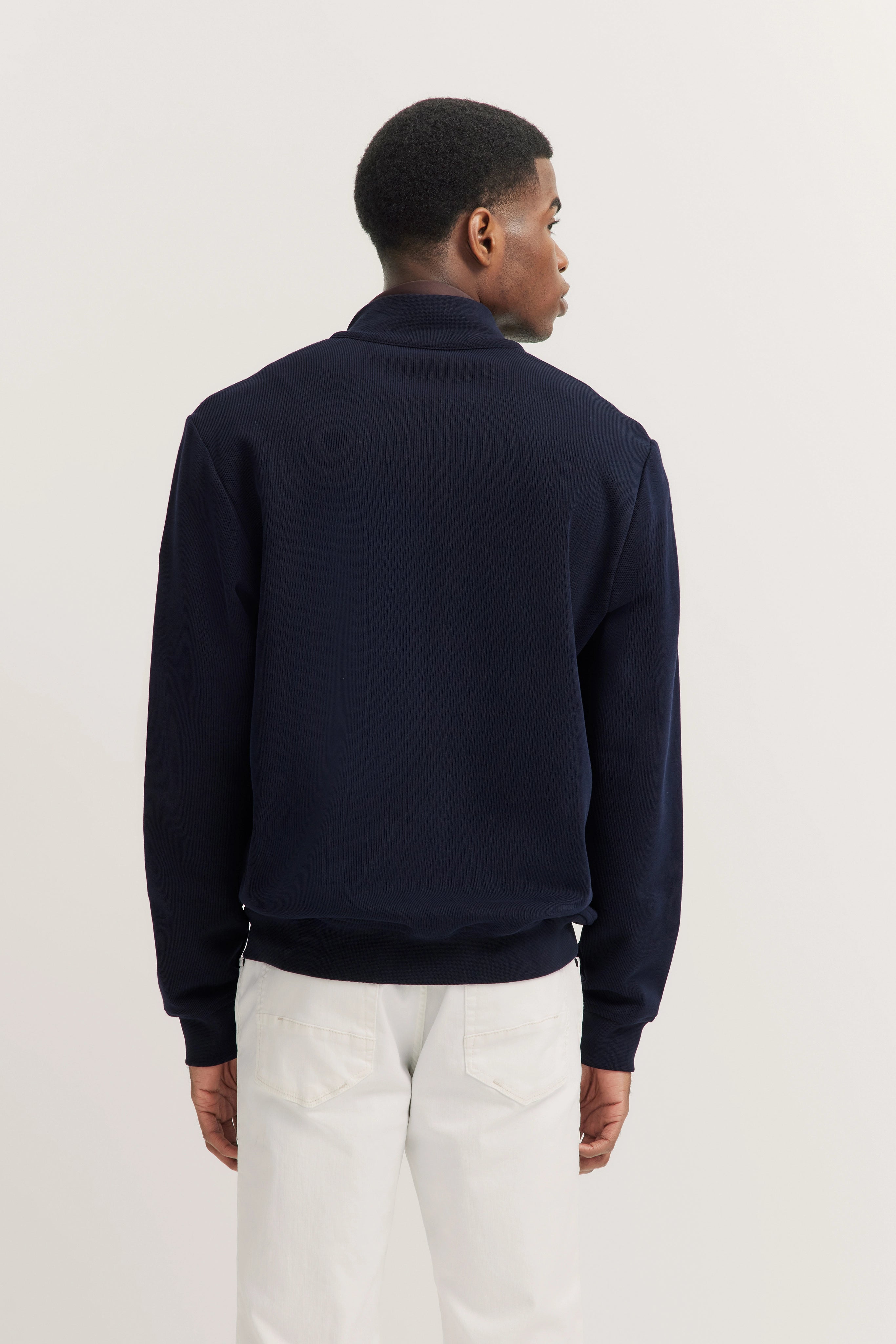 bugatti outfit: Dark blue jacket, white pants, model from behind, relaxed stance.