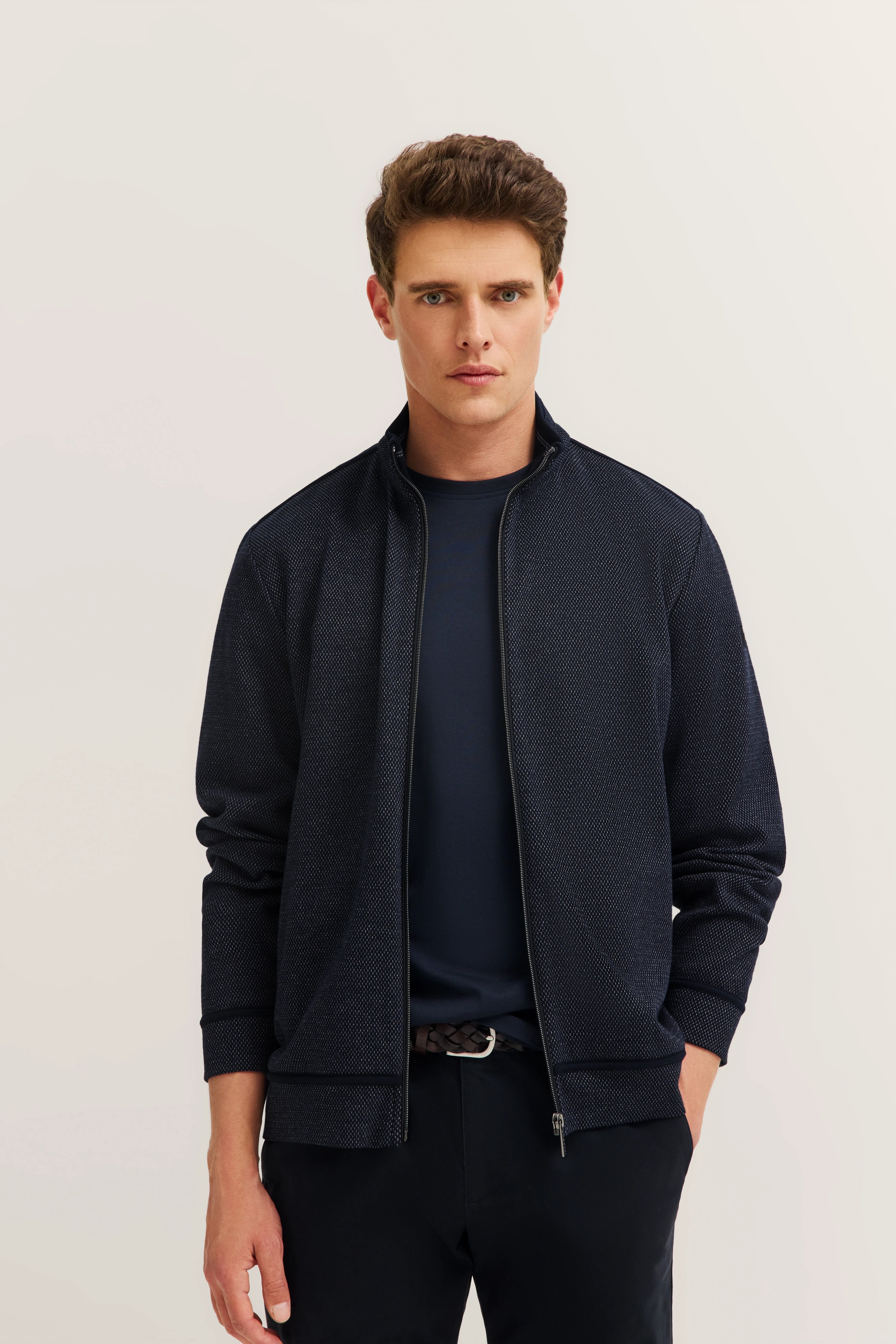 bugatti Model trägt dunkelblauen Blouson mit feinem Muster, darunter ein navy Shirt. Legeres Standposing.