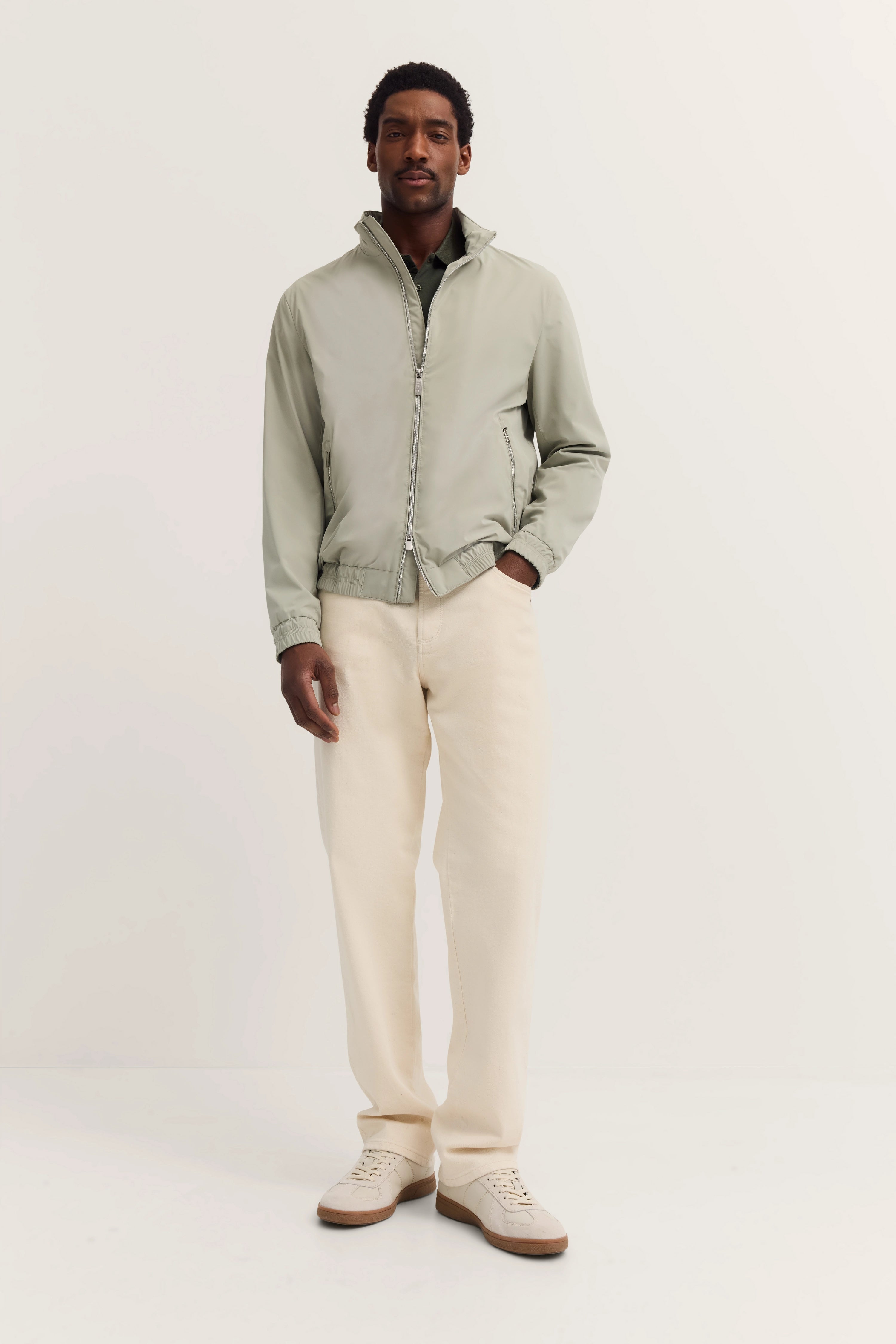 Model in lichtgrijs bugatti-jack, beige broek, ontspannen pose.