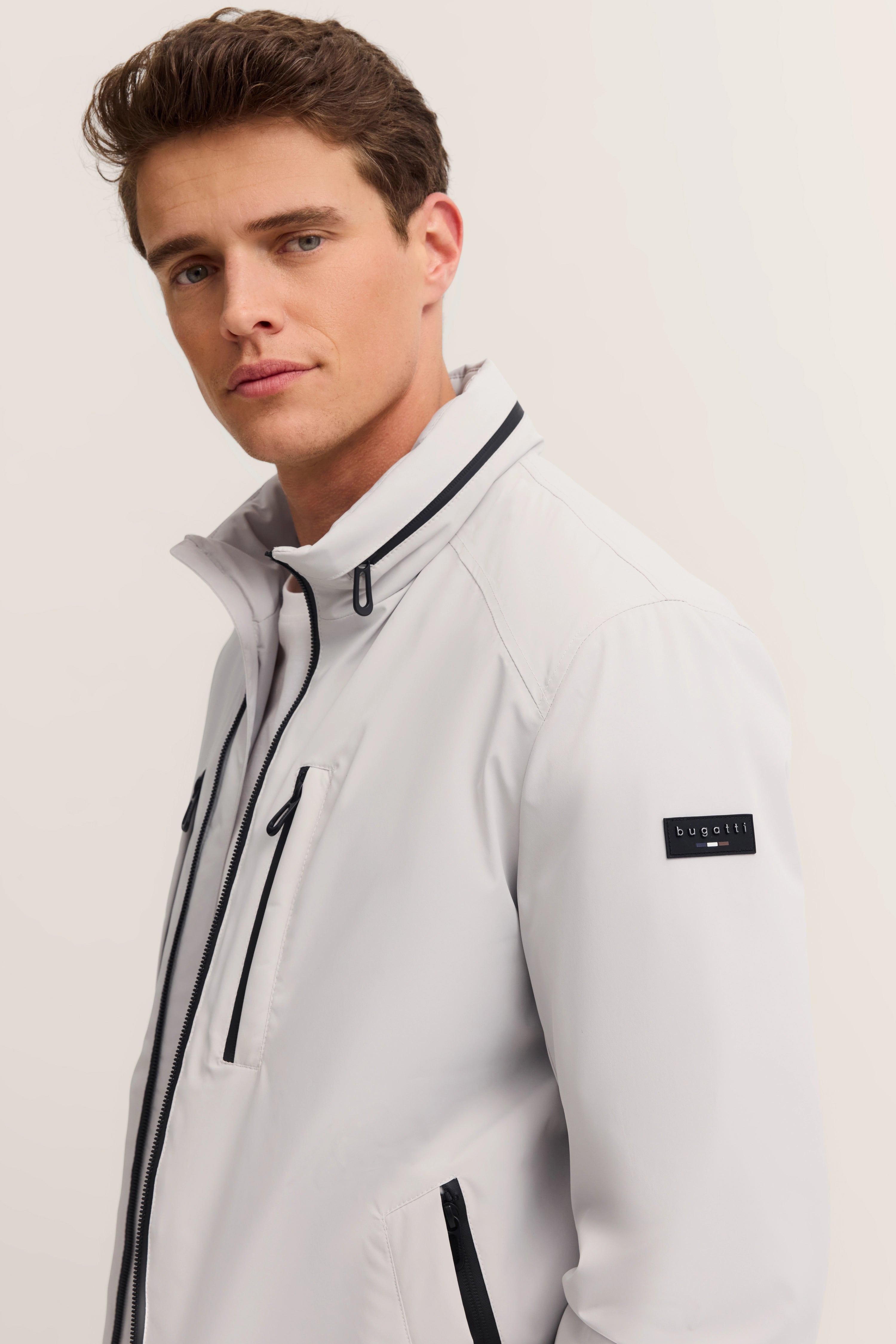 Weiße bugatti Jacke mit schwarzem Reißverschluss auf Model, Halbprofil-Pose.