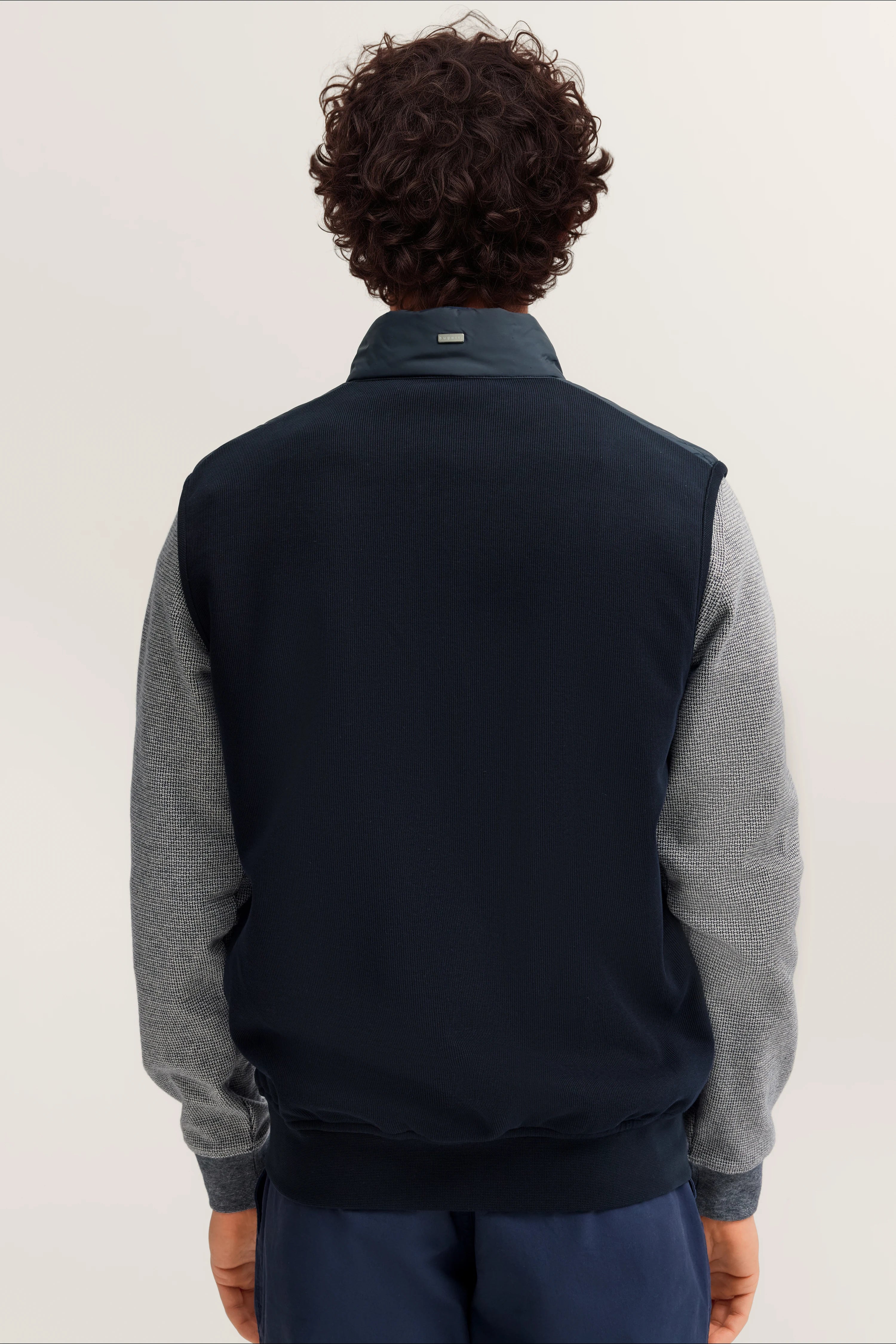 bugatti Herren-Model in marineblauer Jacke mit grauen Ärmeln, Rückenansicht.