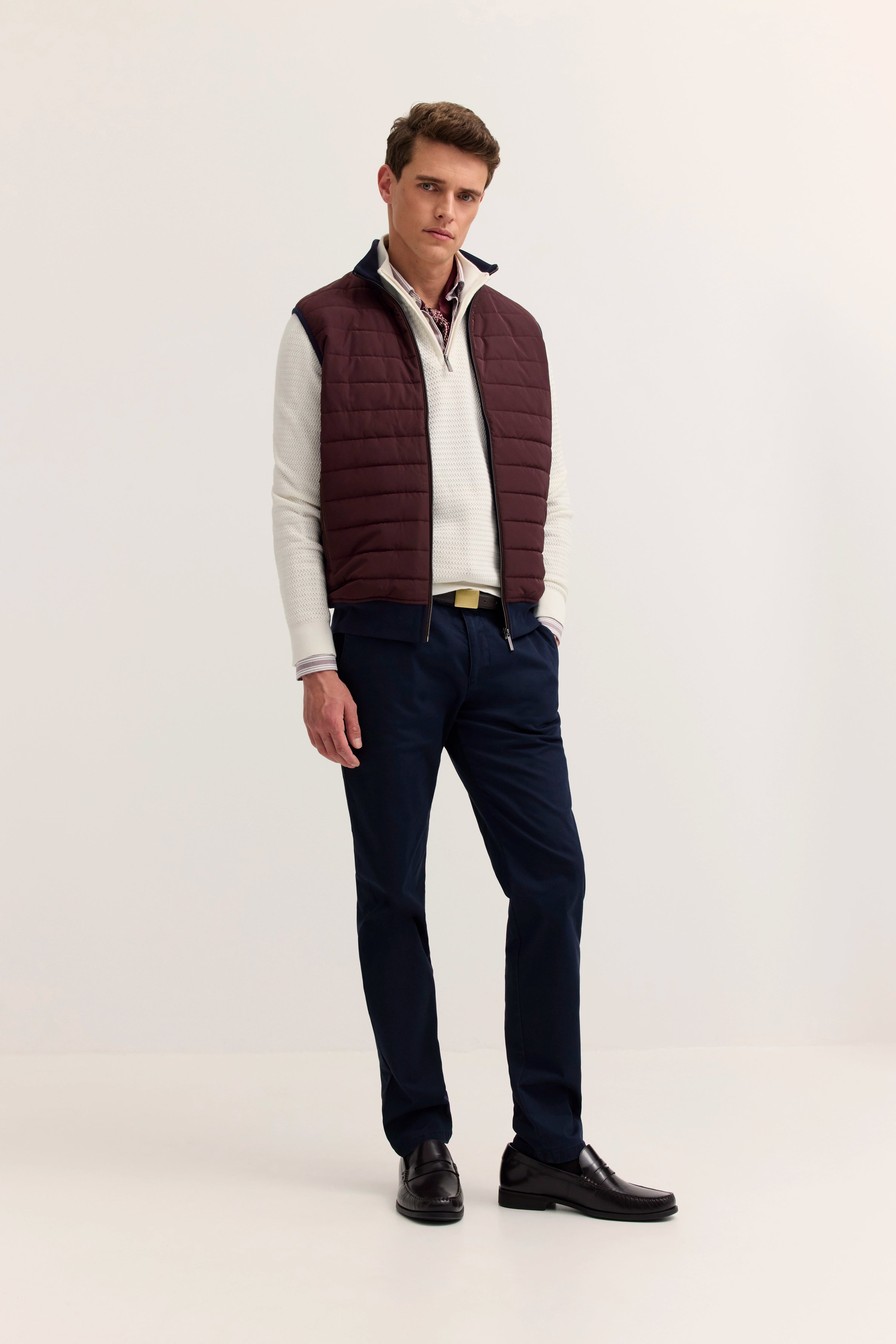Model in burgunder Weste, weißem Pullover, dunkelblauer Hose