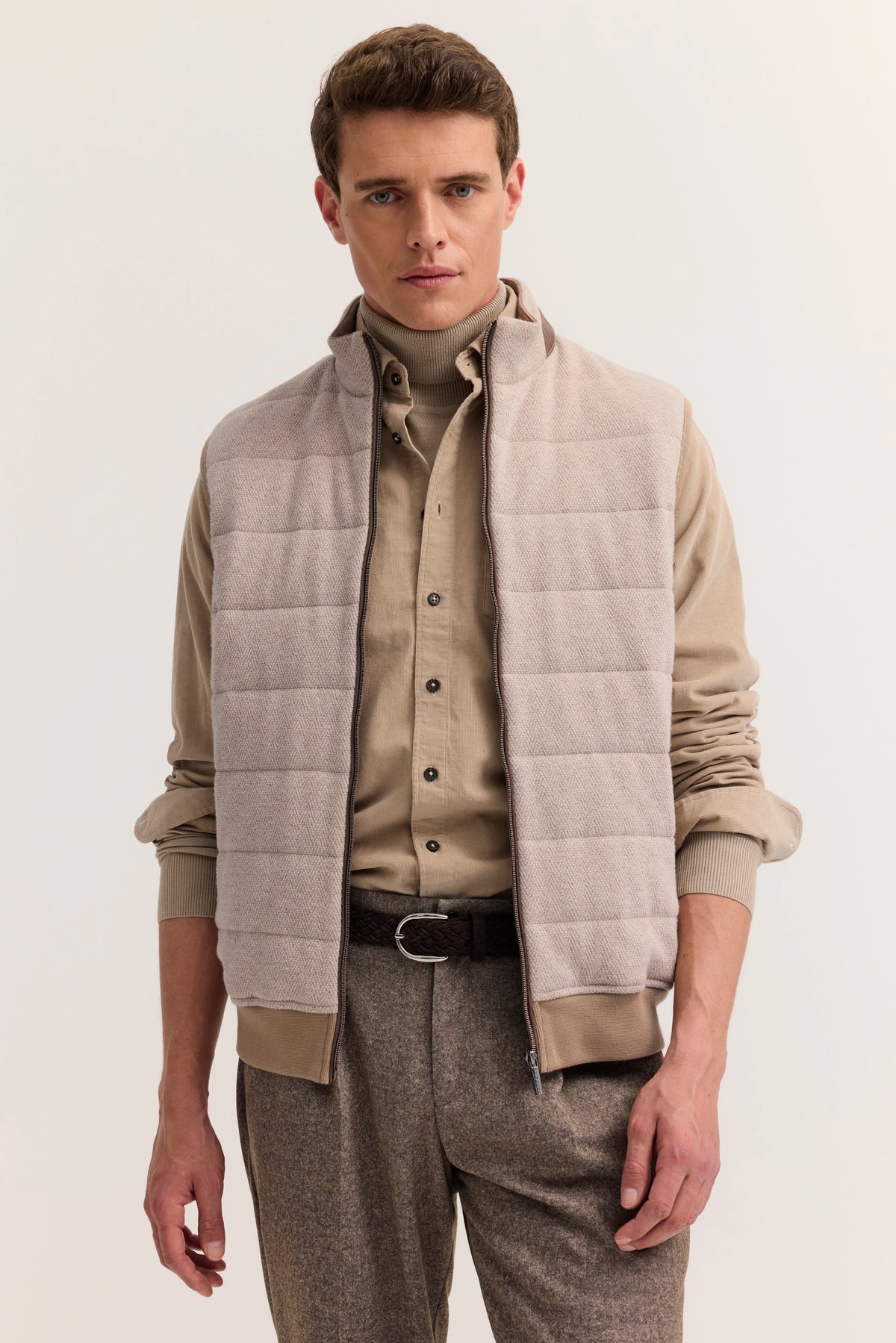Herrenoutfit mit beiger Weste, Hemd und Rollkragen, Modellbild mit lässiger Haltung.