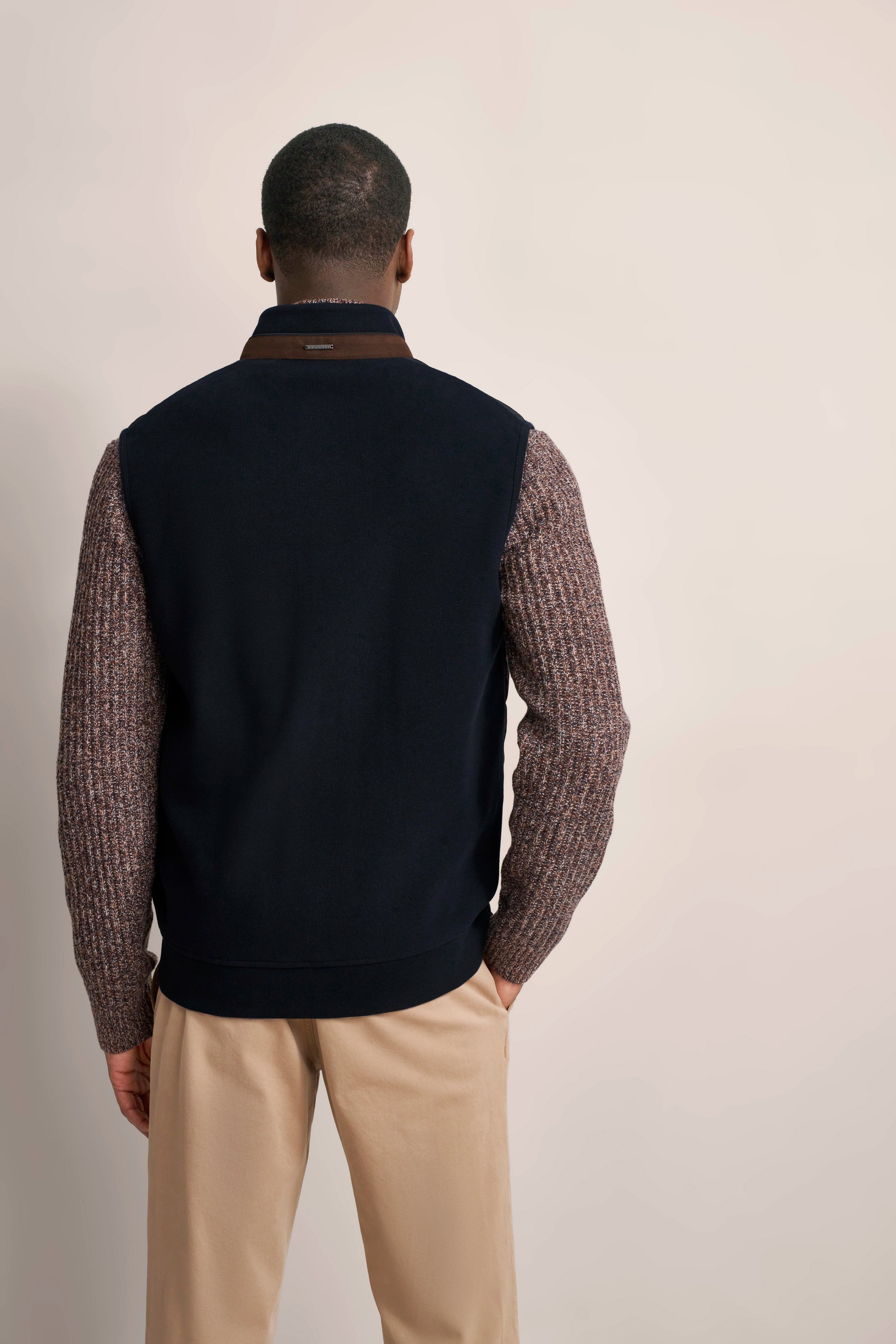 Rückansicht Model beige Hose, navy Weste, braune Strickärmel, legeres Posing.