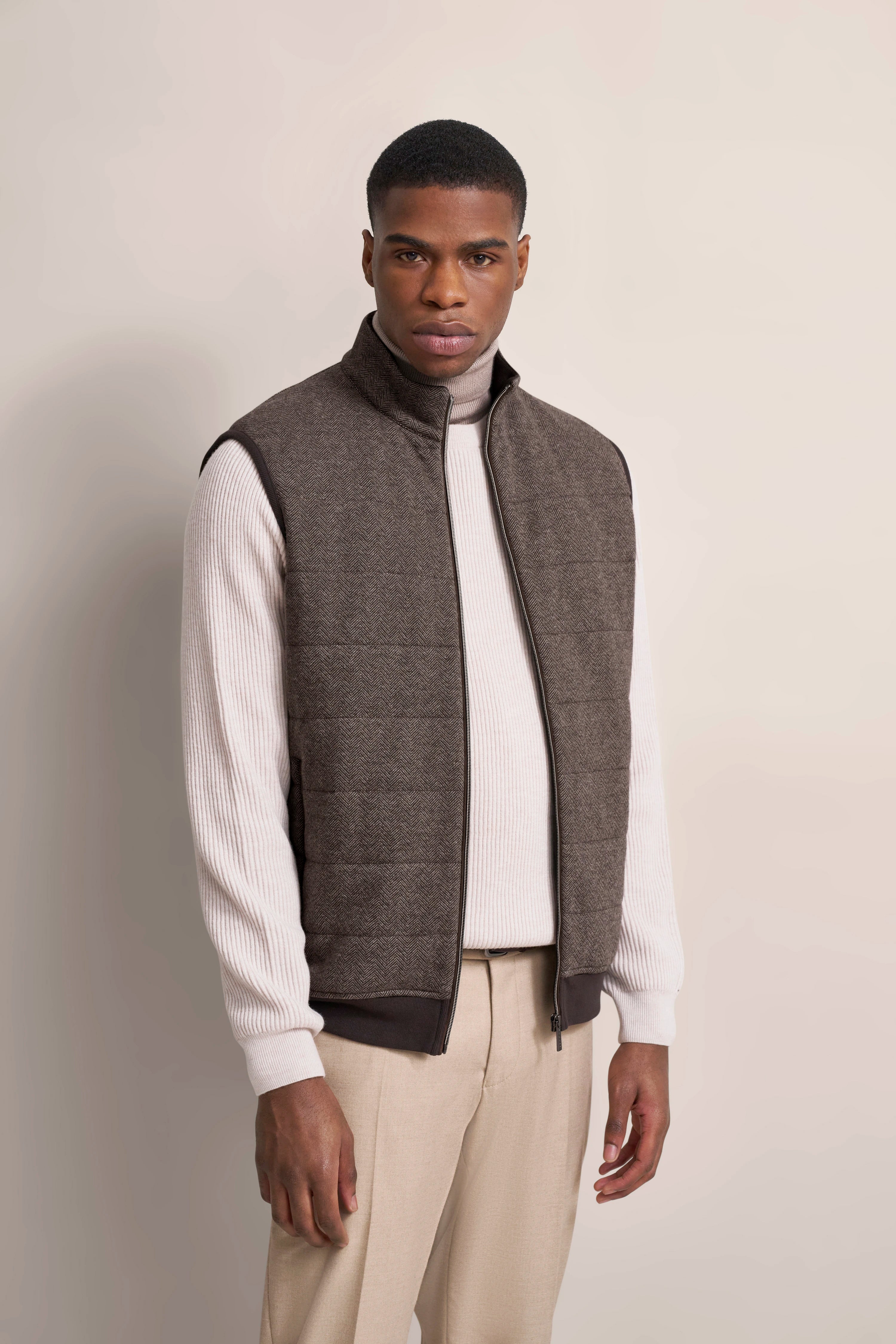 Model in beige Hose, weißem Rollkragenpullover, brauner Weste