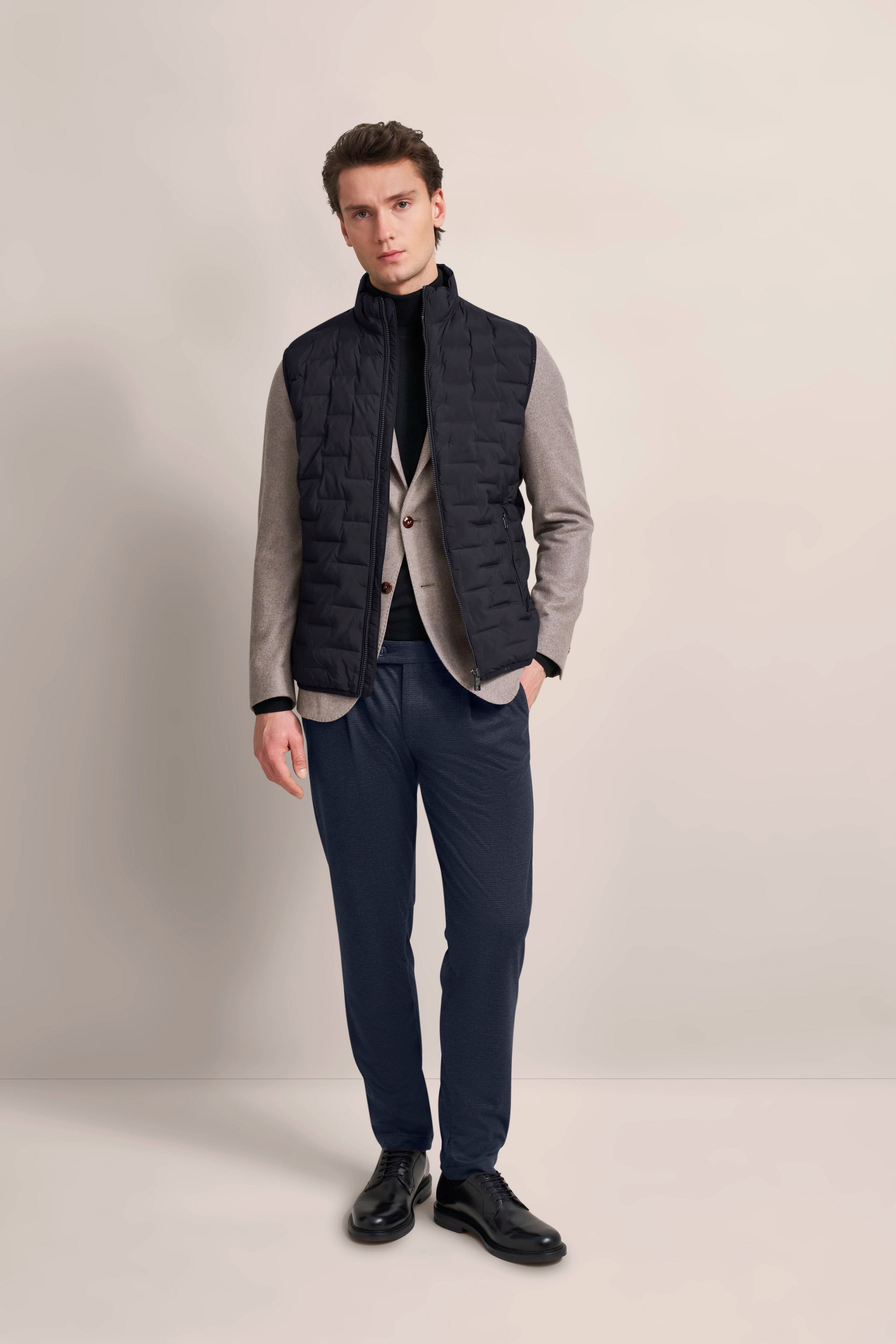 Rückansicht eines Model mit bugatti gesteppter Weste in Schwarz über beigem Blazer, lässig-elegant.