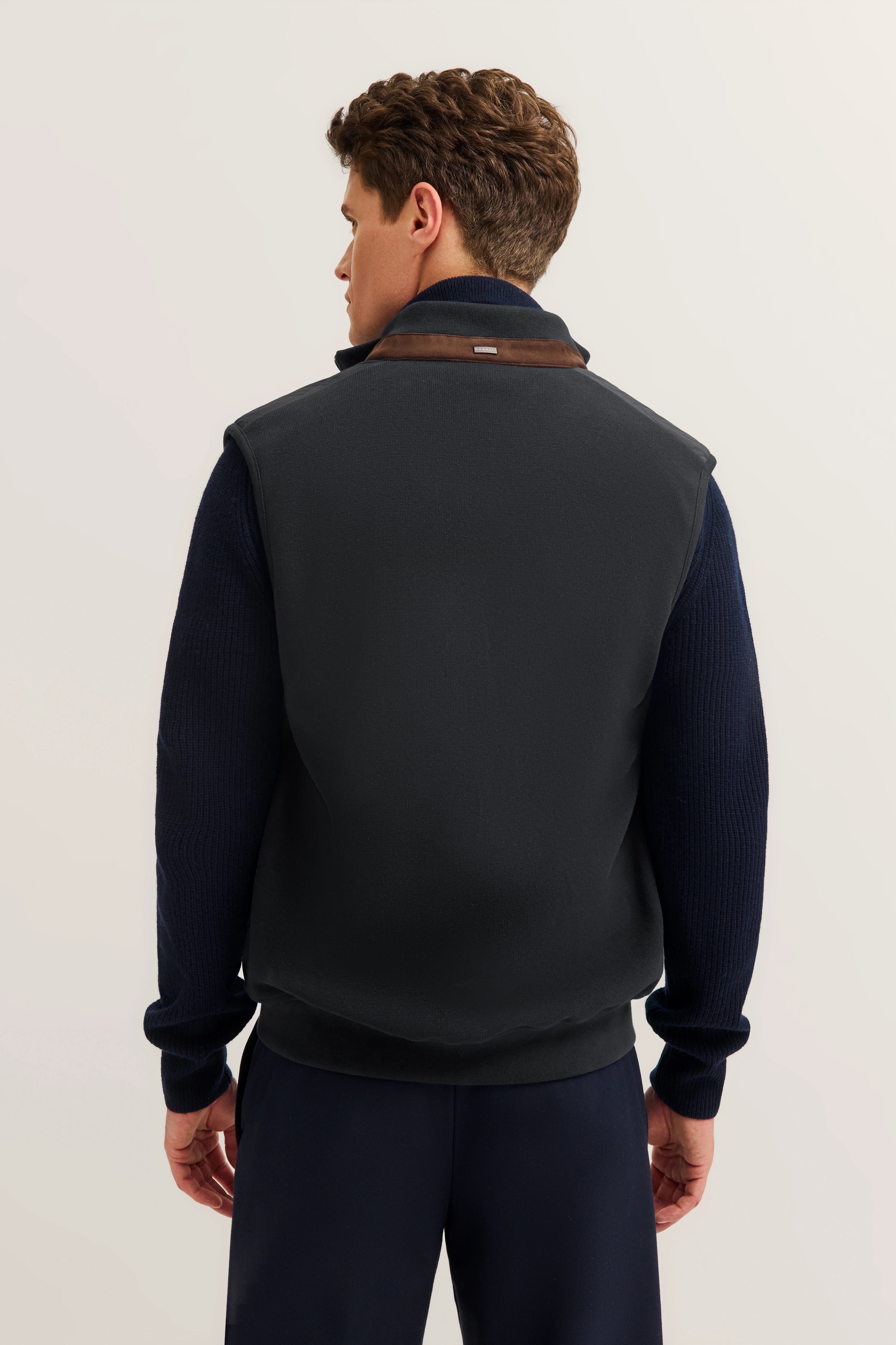 bugatti Model in dunkelblauer Weste und Pullover von hinten, leger stehend, stilvoll und elegant.