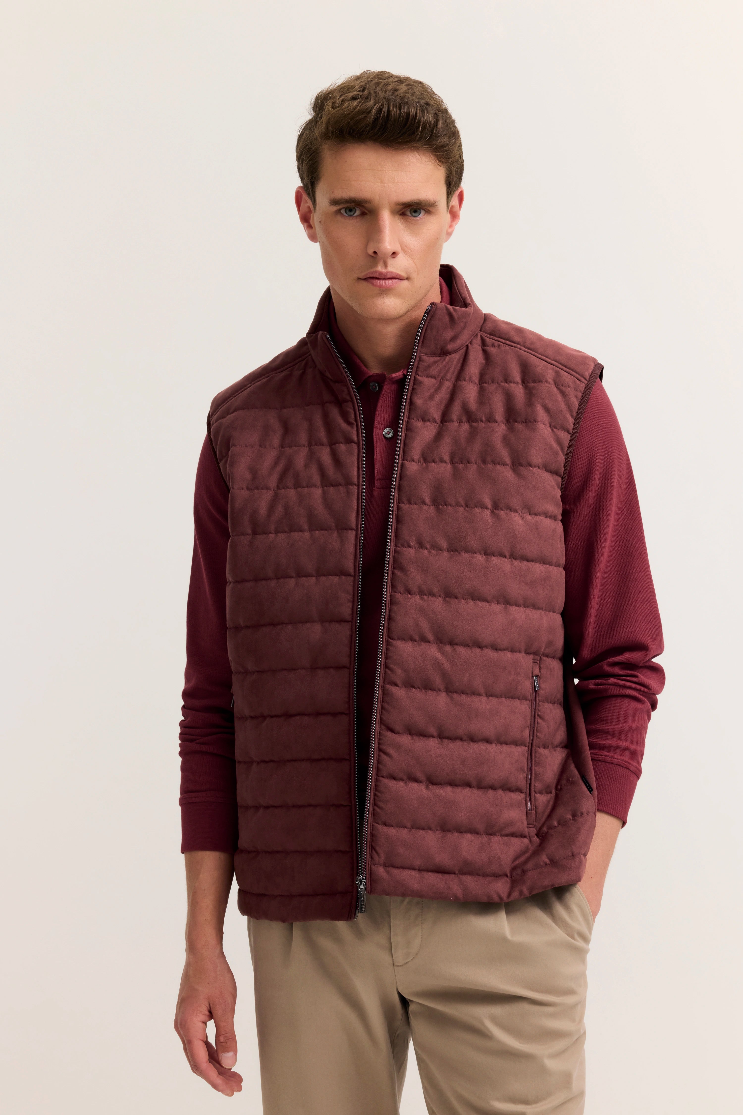 bugatti Modelbild: Mann in bordeauxfarbener Steppweste, passendem Polo und beigen Chinos, frontal stehend.