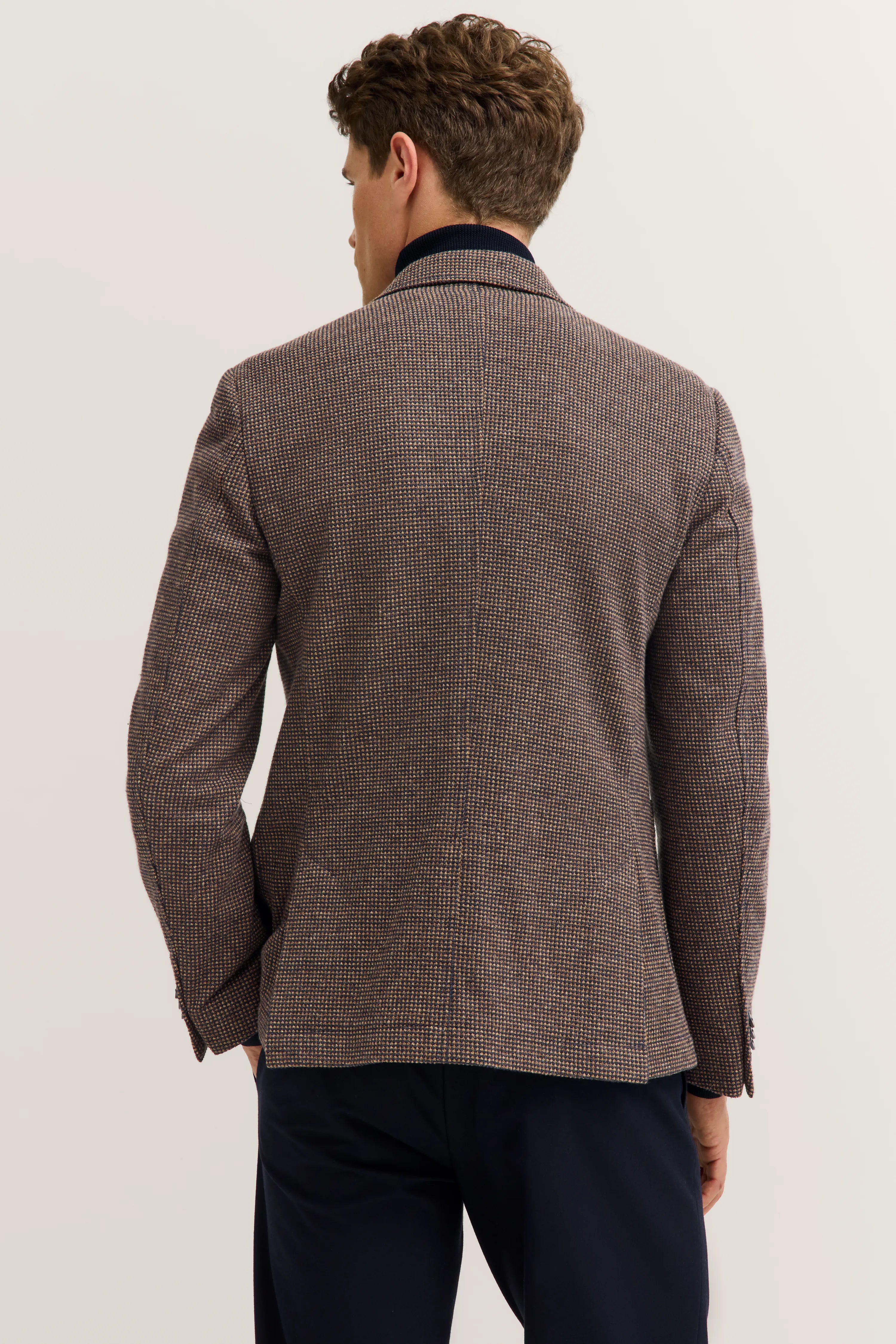 Rückansicht eines Mannes in braunem bugatti Blazer mit feinem Muster, kombiniert mit dunkelblauer Hose.