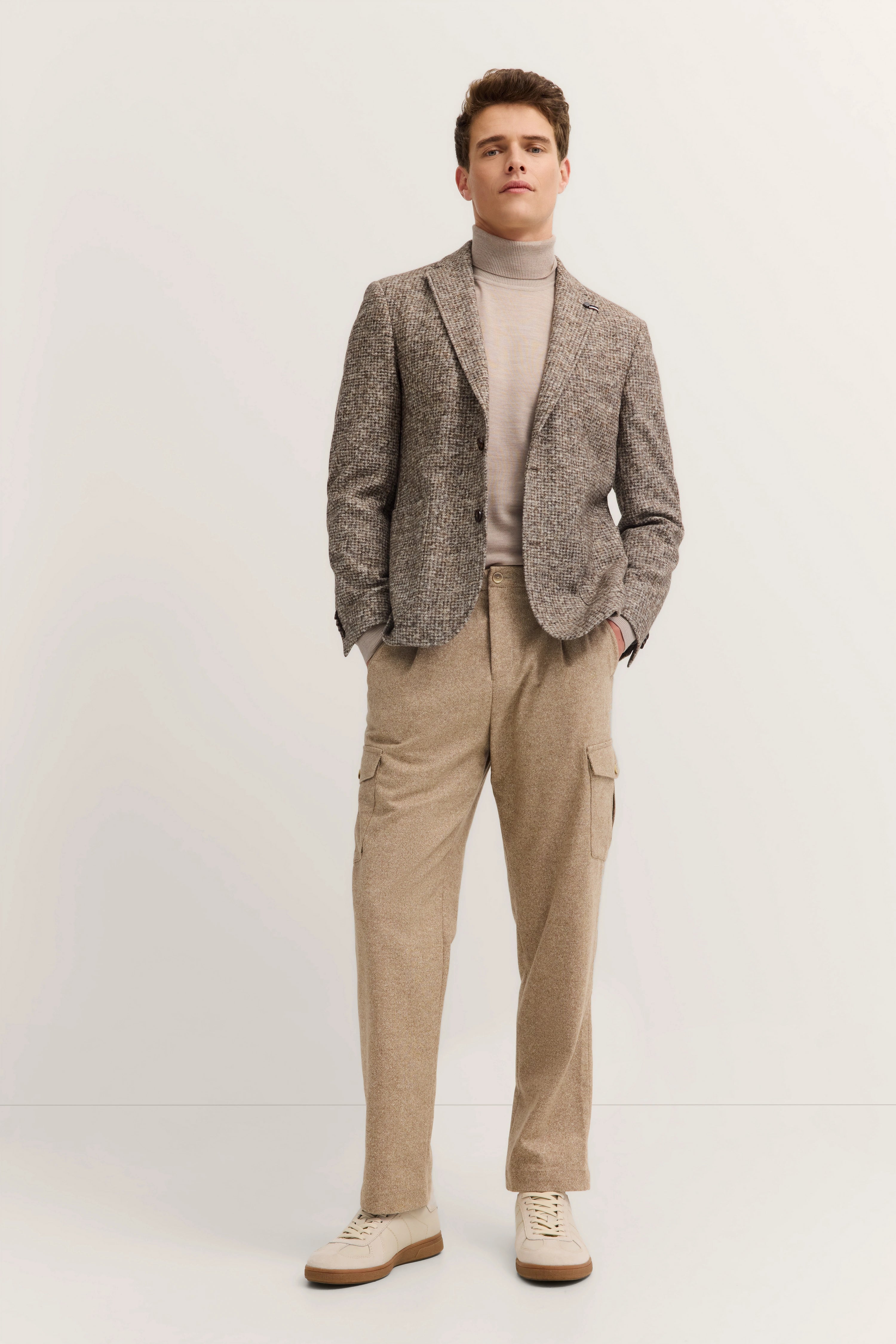 Model in beigem Rollkragen, grauem Sakko und beigen Hosen von bugatti, lässige Pose.