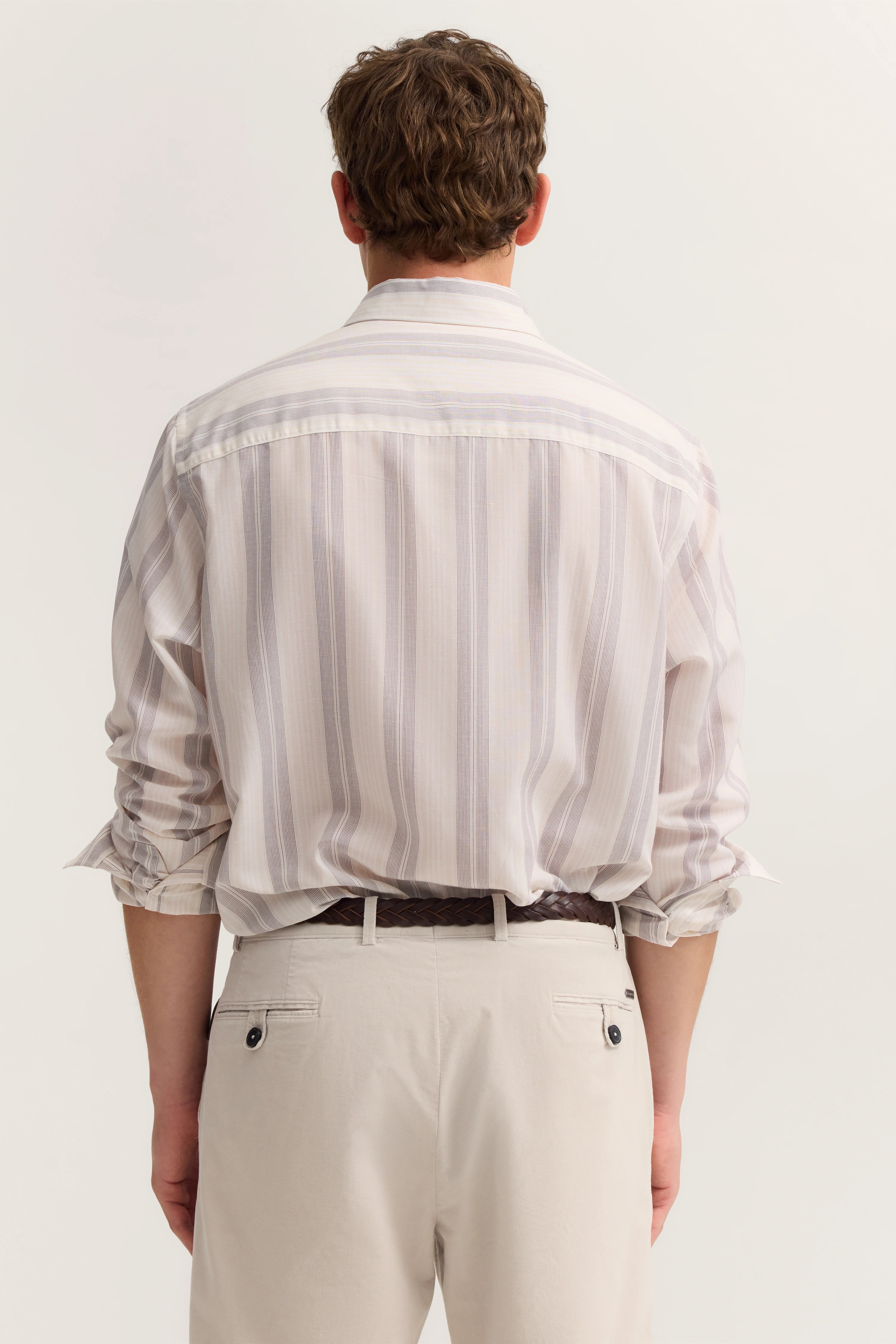 bugatti Modelbild, gestreiftes Hemd in Beige und Weiß mit beigen Hosen, Rückenansicht, entspannte Pose.