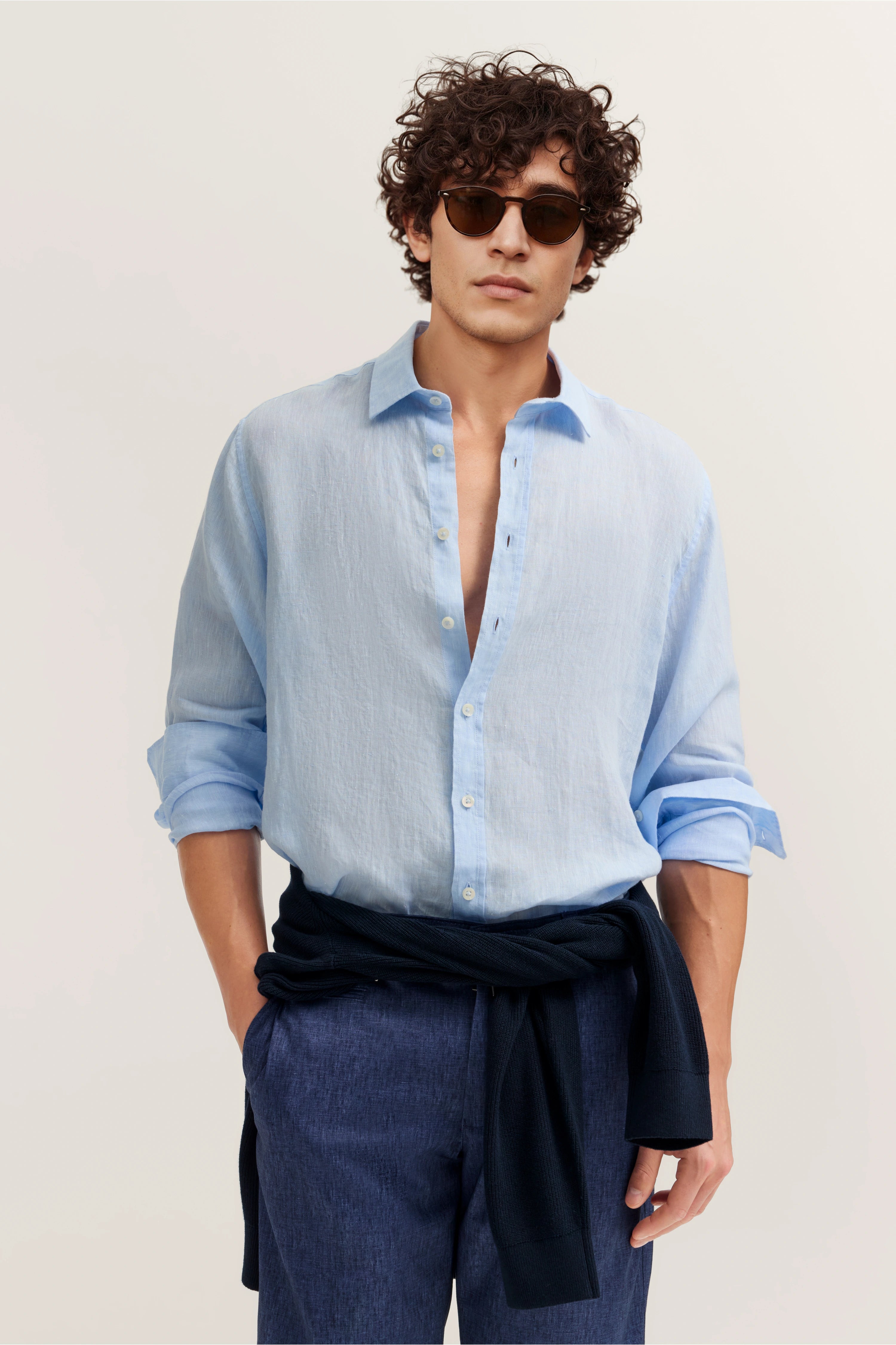 Model in hellem, offenem Hemd, dunkelblaue Hose, Pullover um die Taille, lässige Pose.