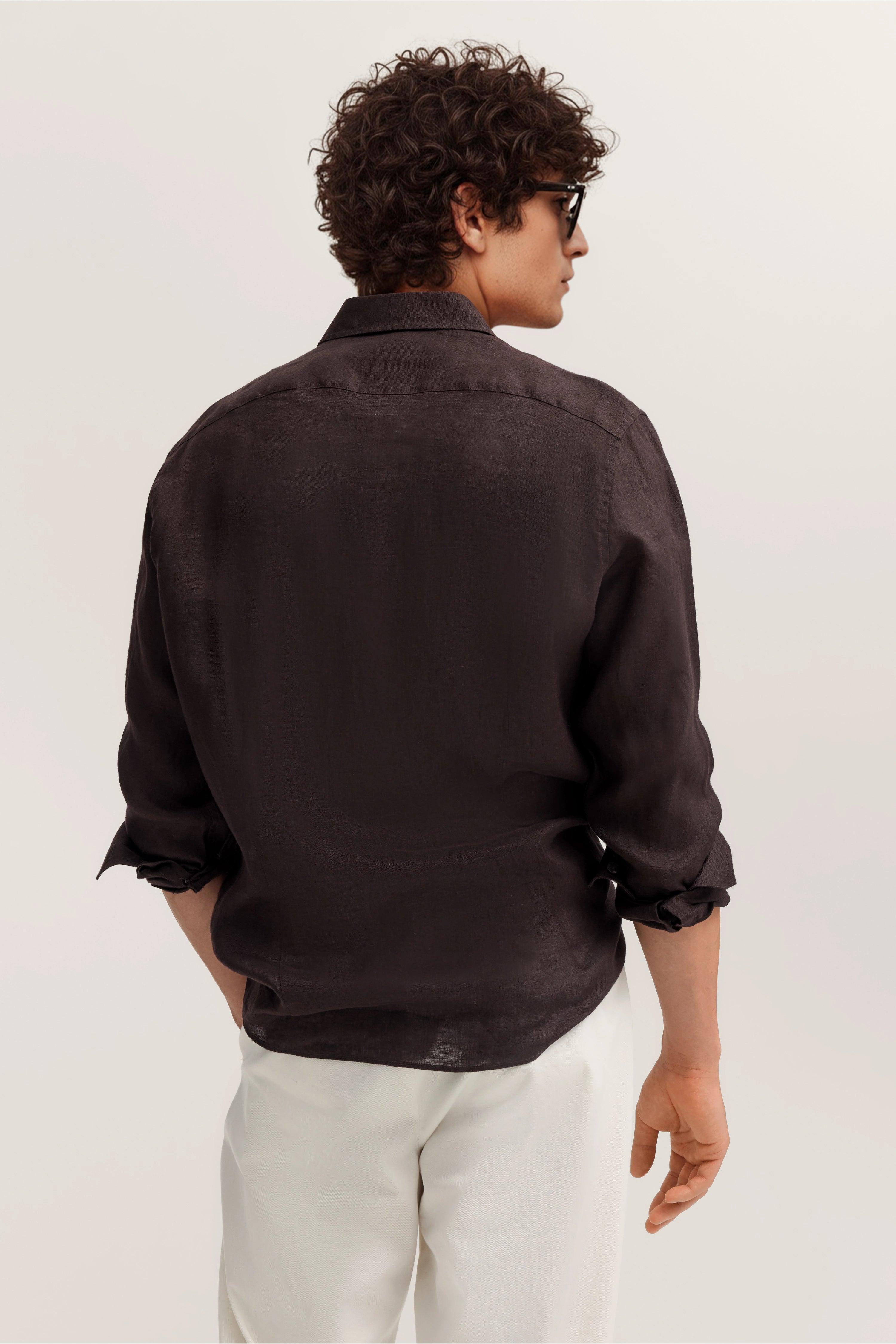 Model trägt dunkles Hemd und weiße Hose von bugatti, leger von hinten, Arme entspannt in Taschen.