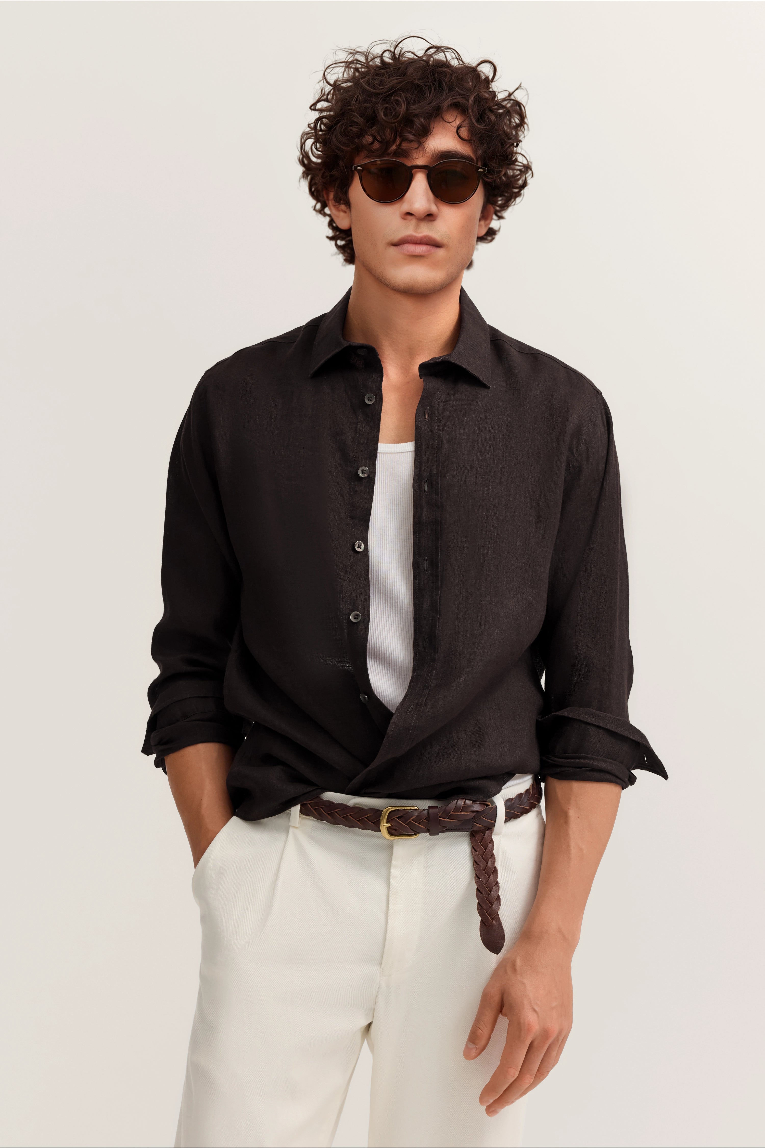 Model mit schwarzem Hemd, weißem Tanktop, weißer Hose, braunem Gürtel, lässig posierend.