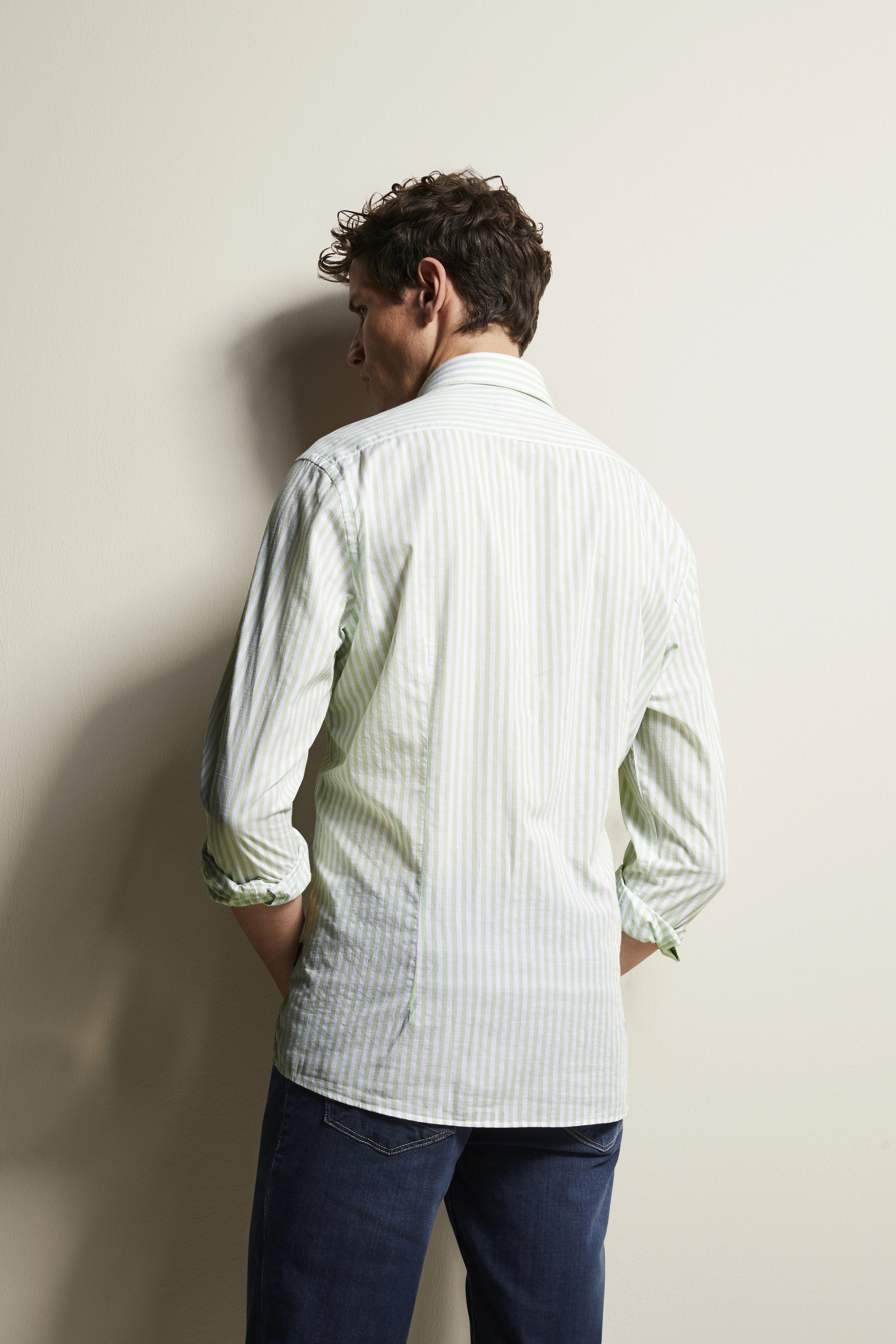 Rückansicht eines Models in grün-weiß gestreiftem bugatti-Hemd, legeres Pose, Jeans.