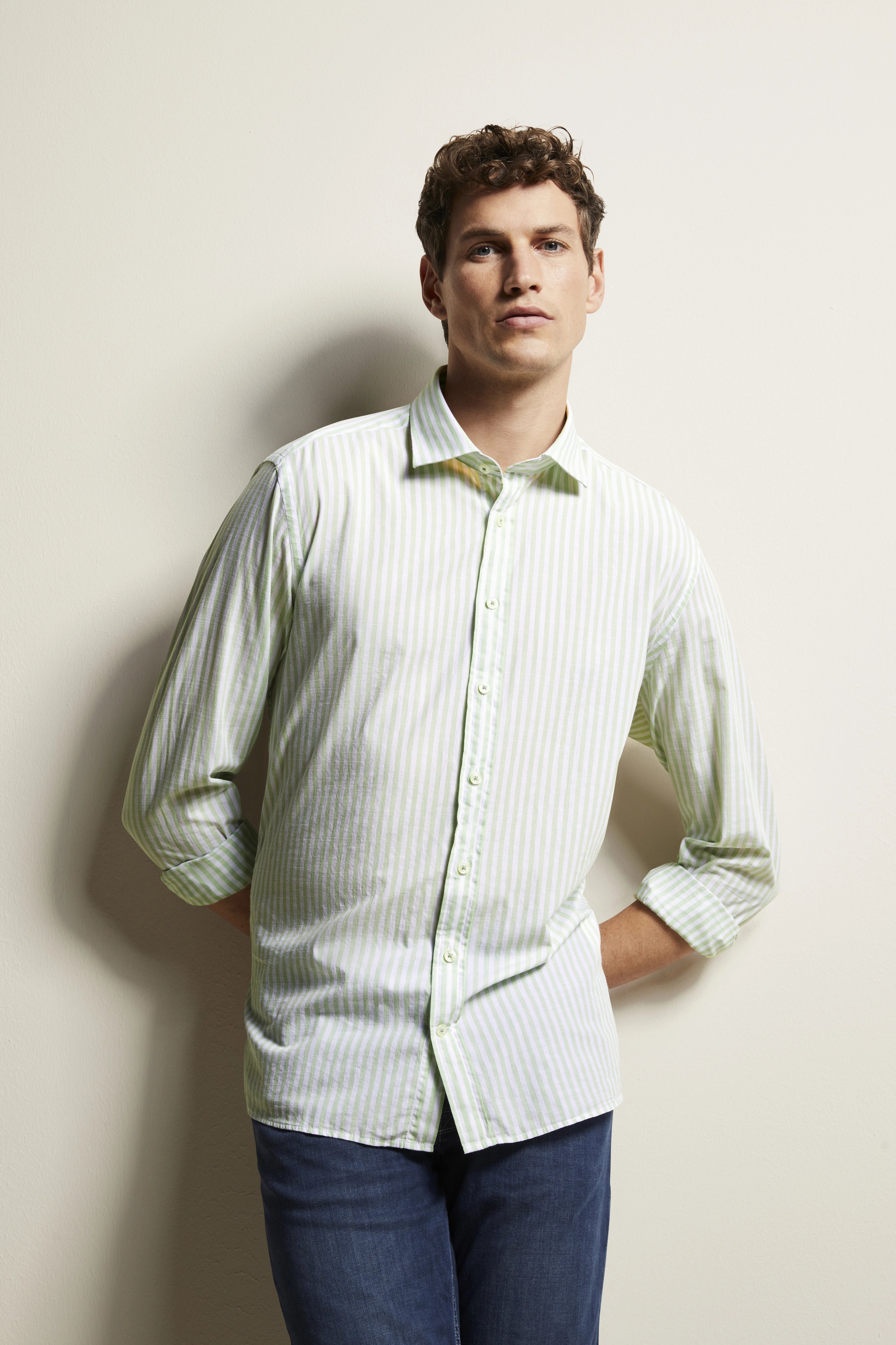 Herr in grün-weiß gestreiftem Hemd von bugatti, lässige Pose, Hände in den Taschen.