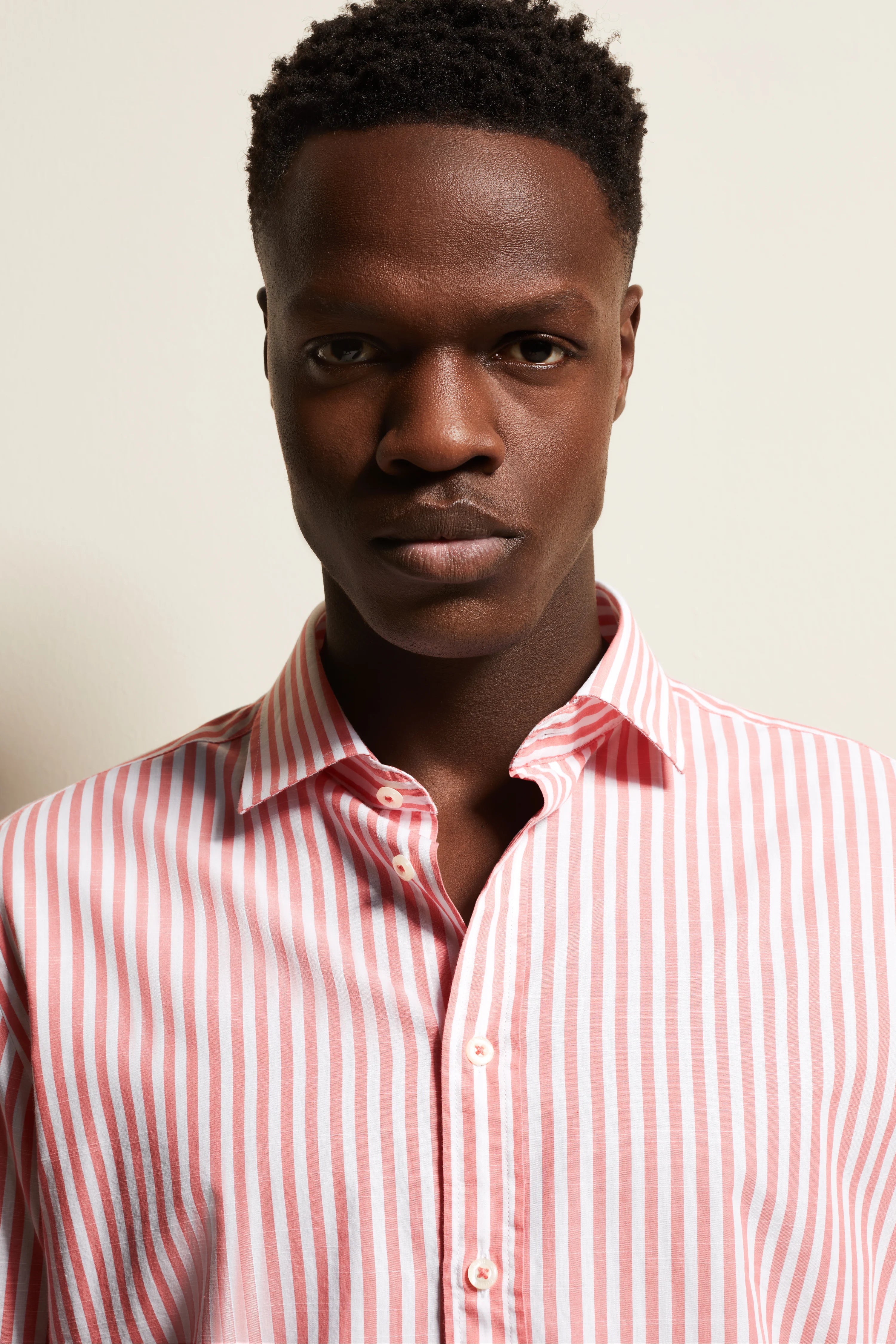 Model in pink-white striped bugatti shirt, front view, casual pose.