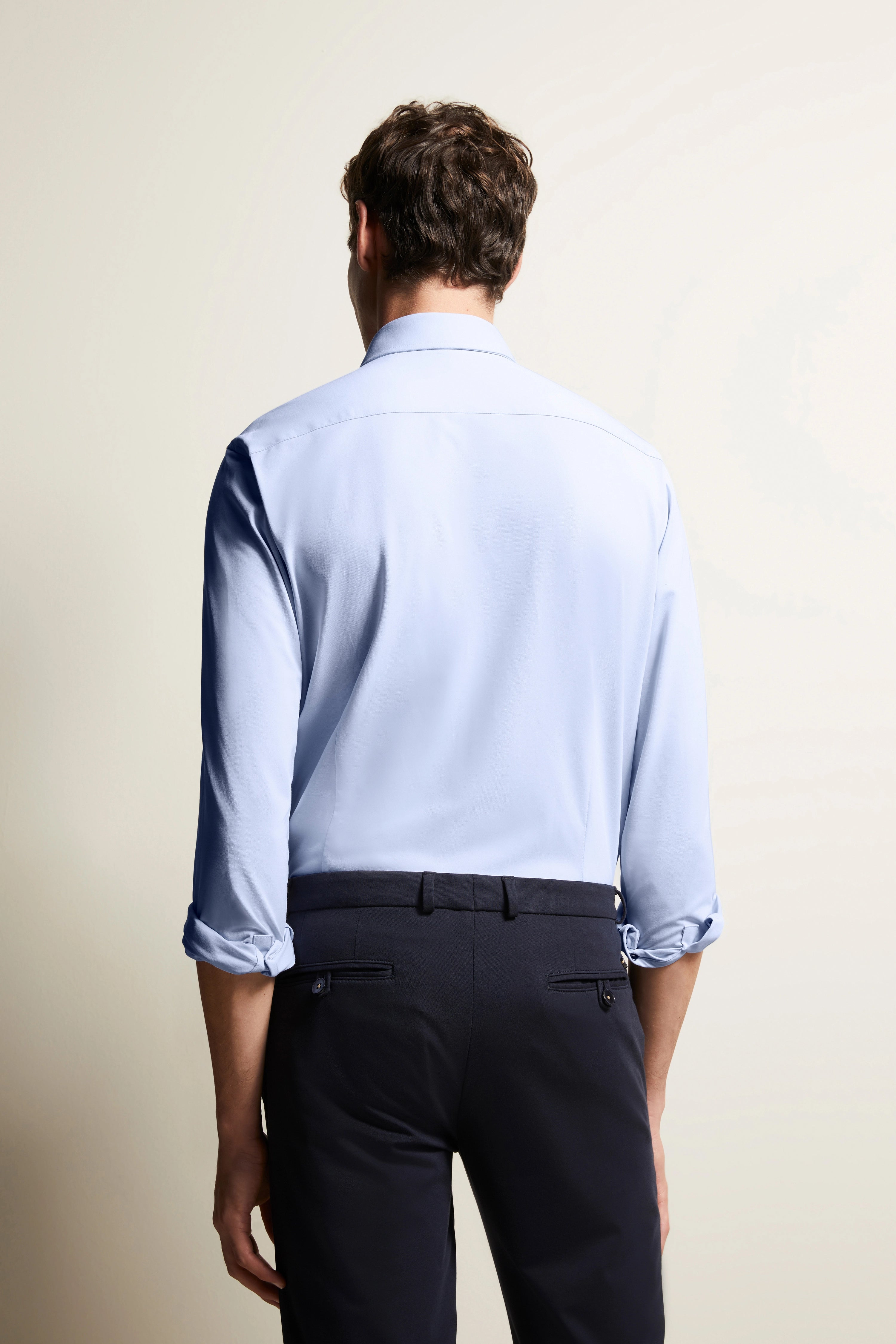 Lichtblauw overhemd met opgerolde mouwen, zwarte broek, rugaanzicht, model staat ontspannen.