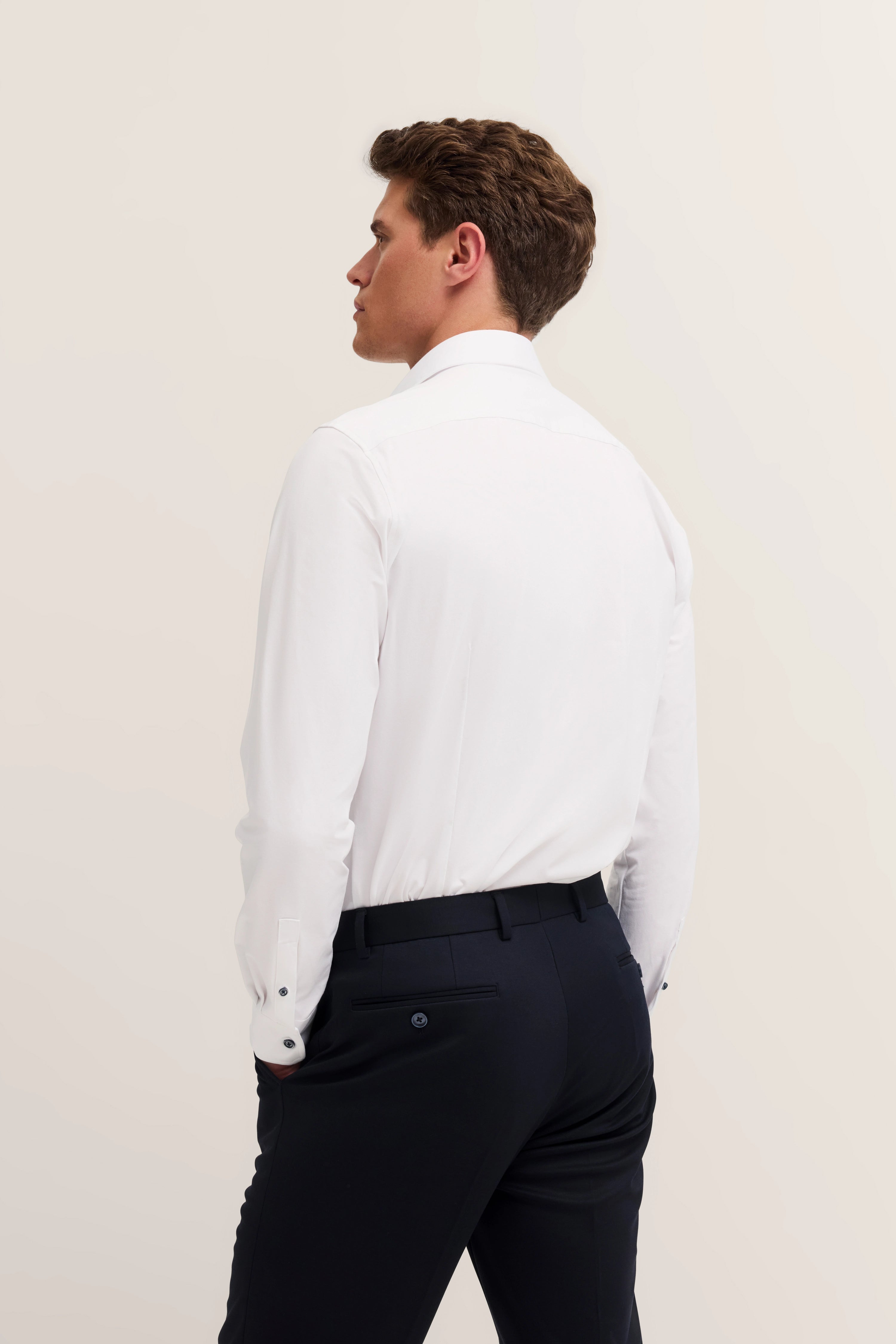 Witte bugatti blouse, zwarte broek, model van achteren, ontspannen hand in broekzak.