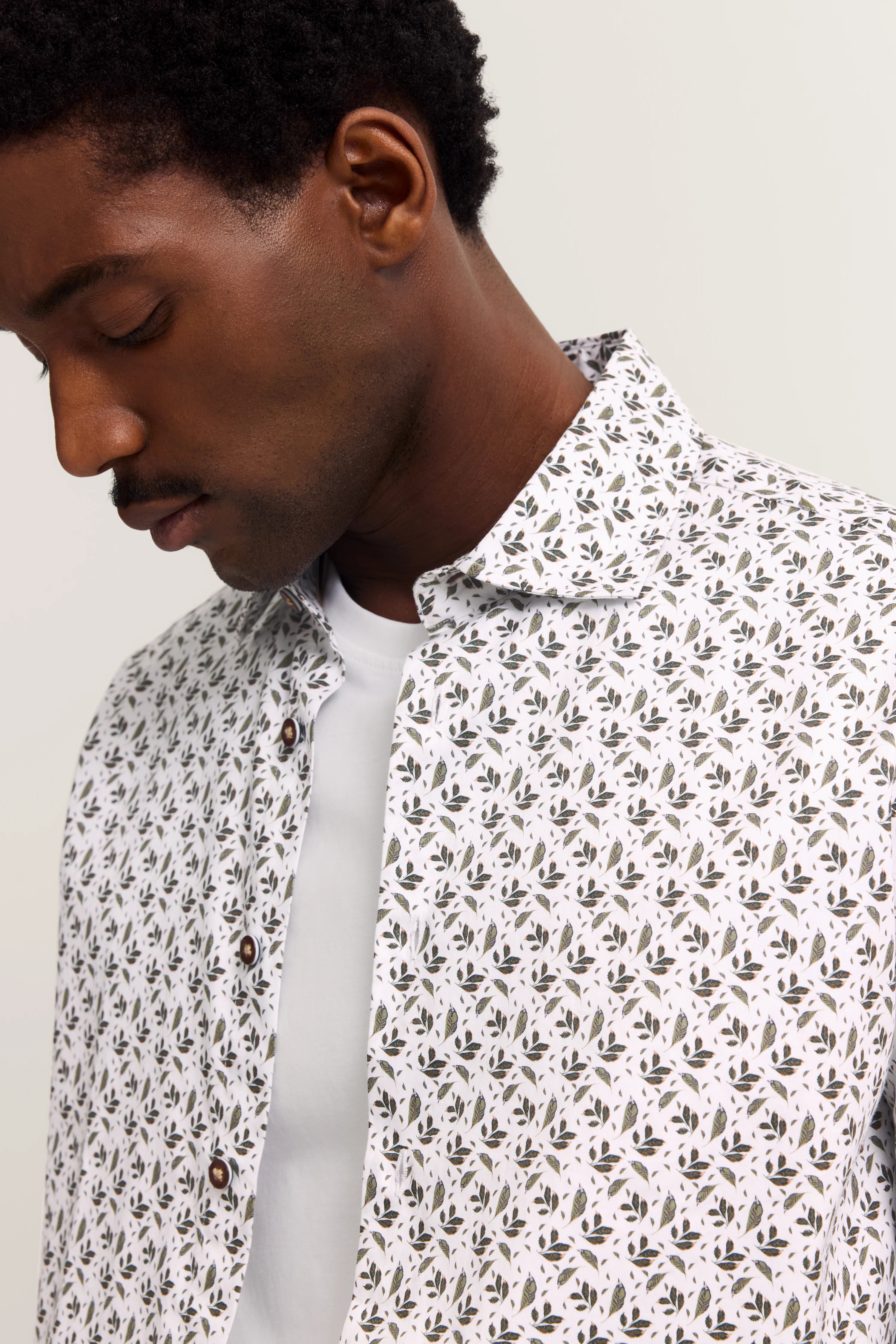 Weißes Hemd mit schwarzem Blattmuster, über weißem Shirt, Modelbild, entspannter Blick nach unten.