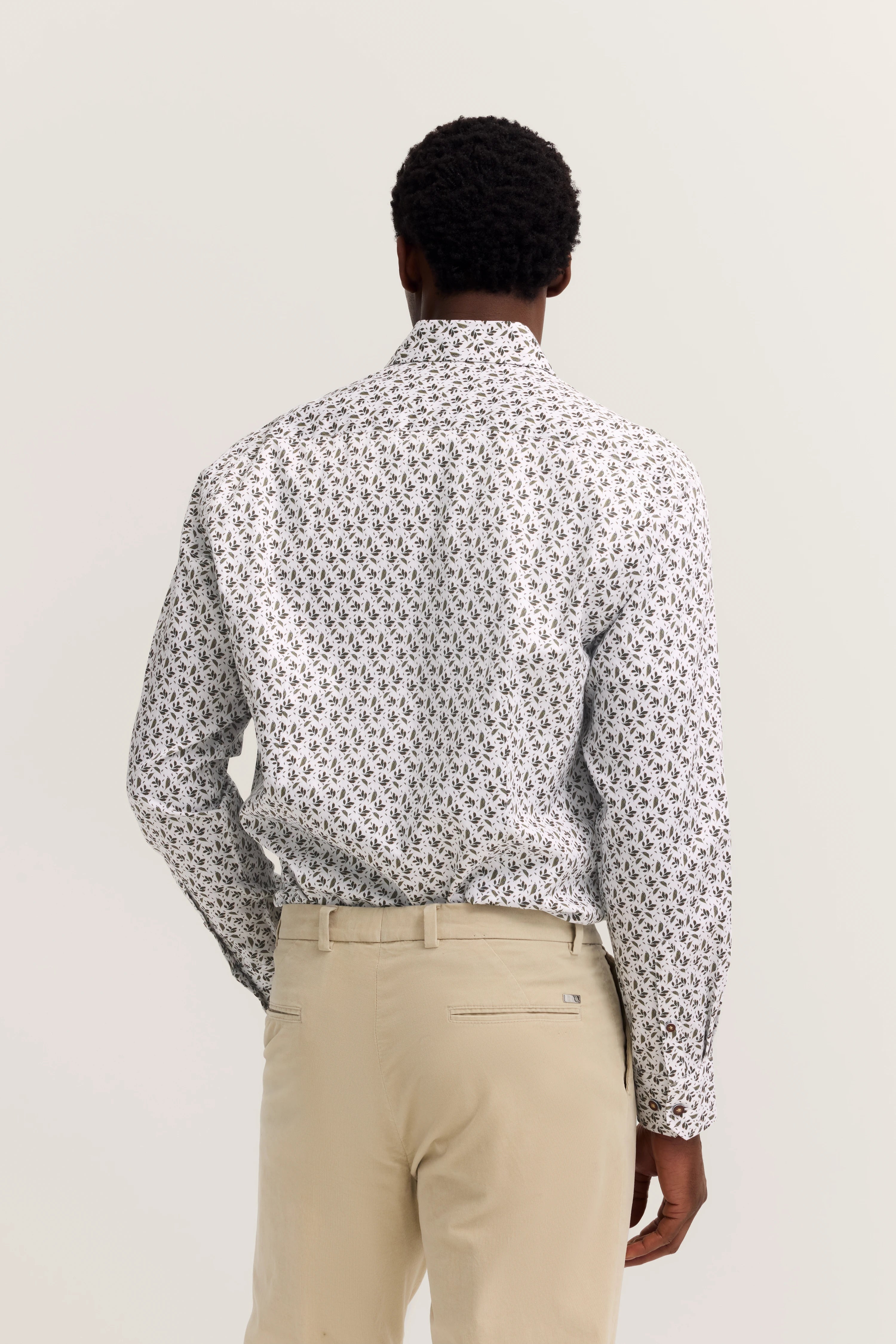 Herrenmodell in gemustertem Hemd und beigen Hosen, von hinten fotografiert.