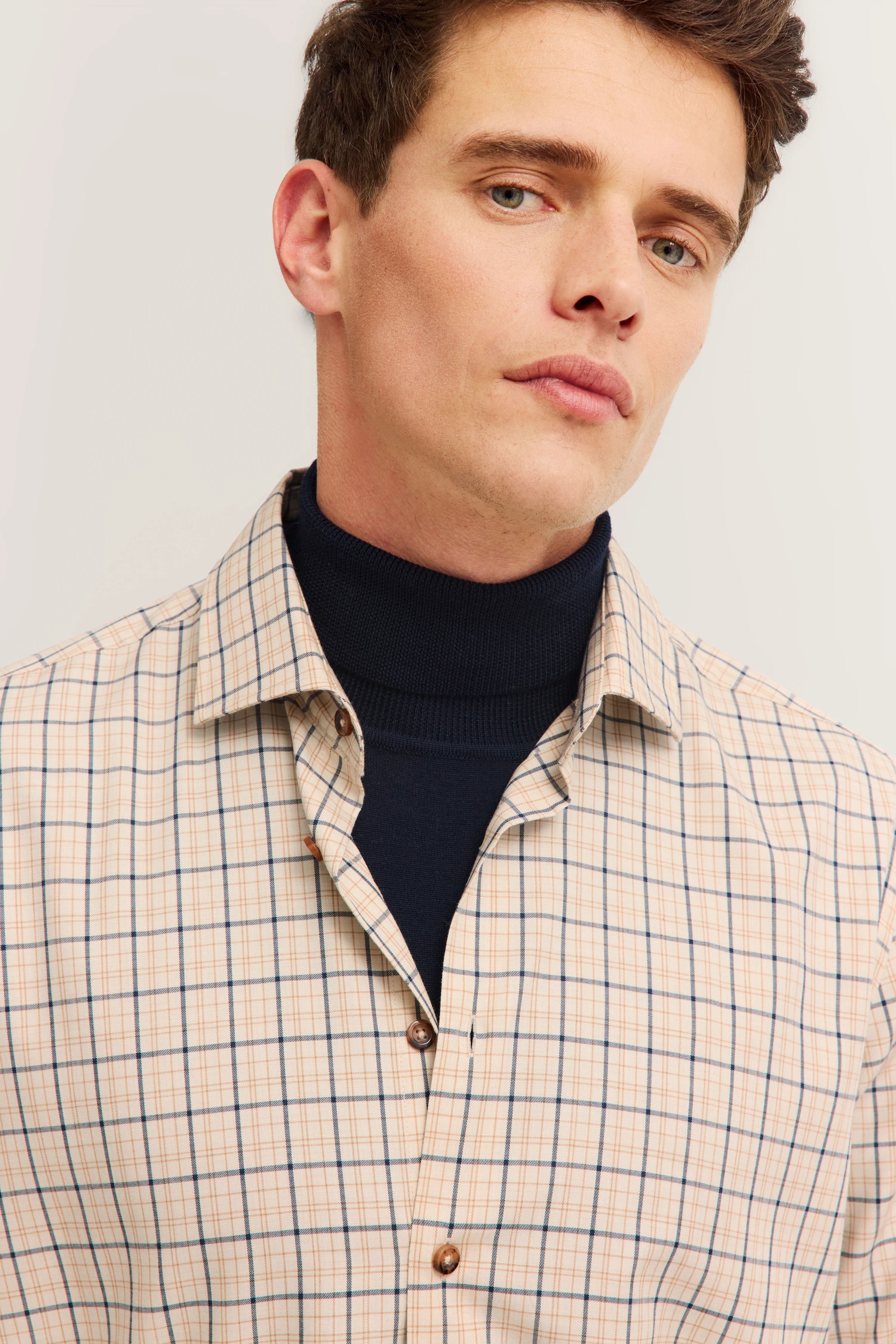 bugatti model wearing beige-blue checkered shirt over dark blue turtleneck sweater.
