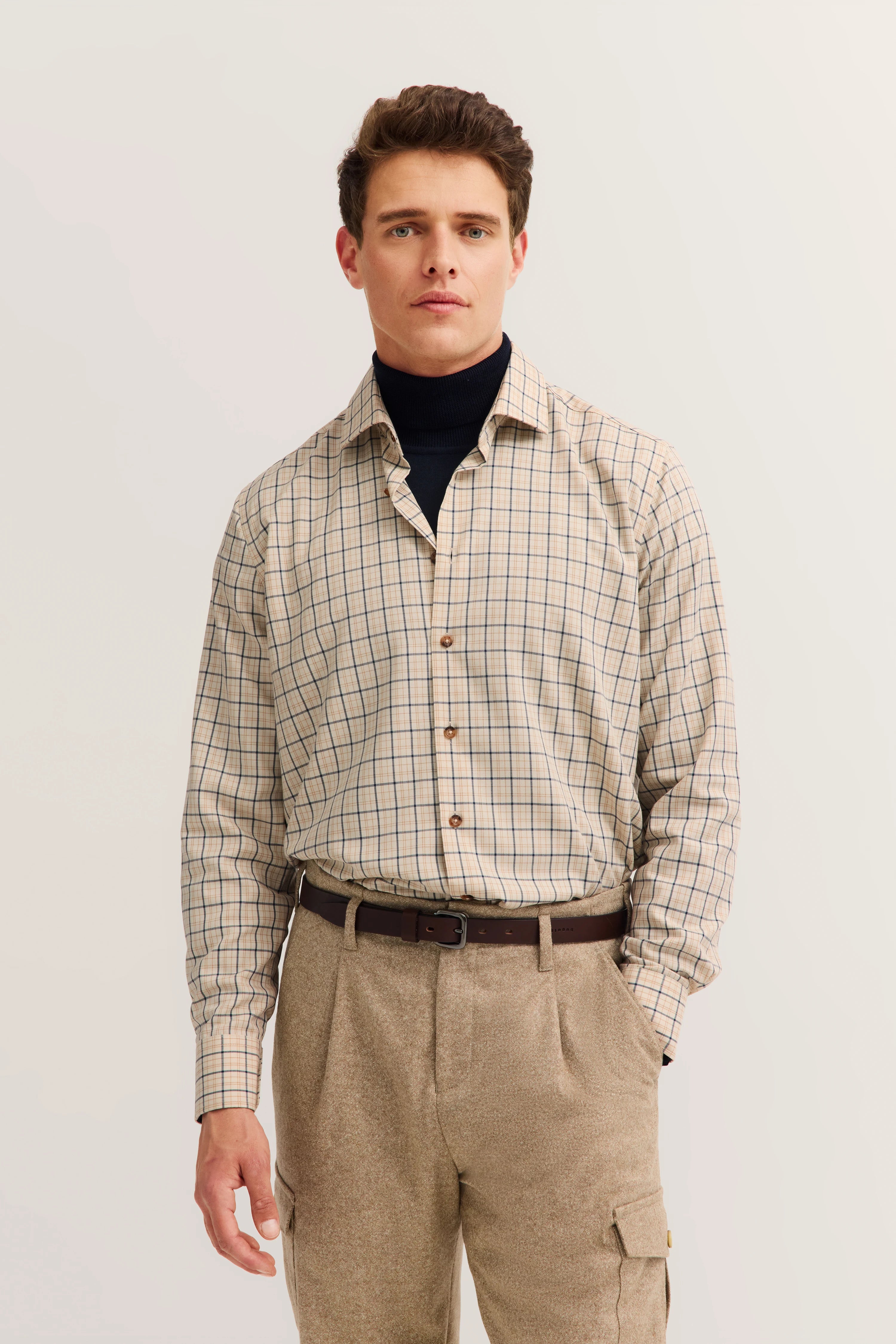Beige check shirt over navy turtleneck, beige trousers, model standing upright.