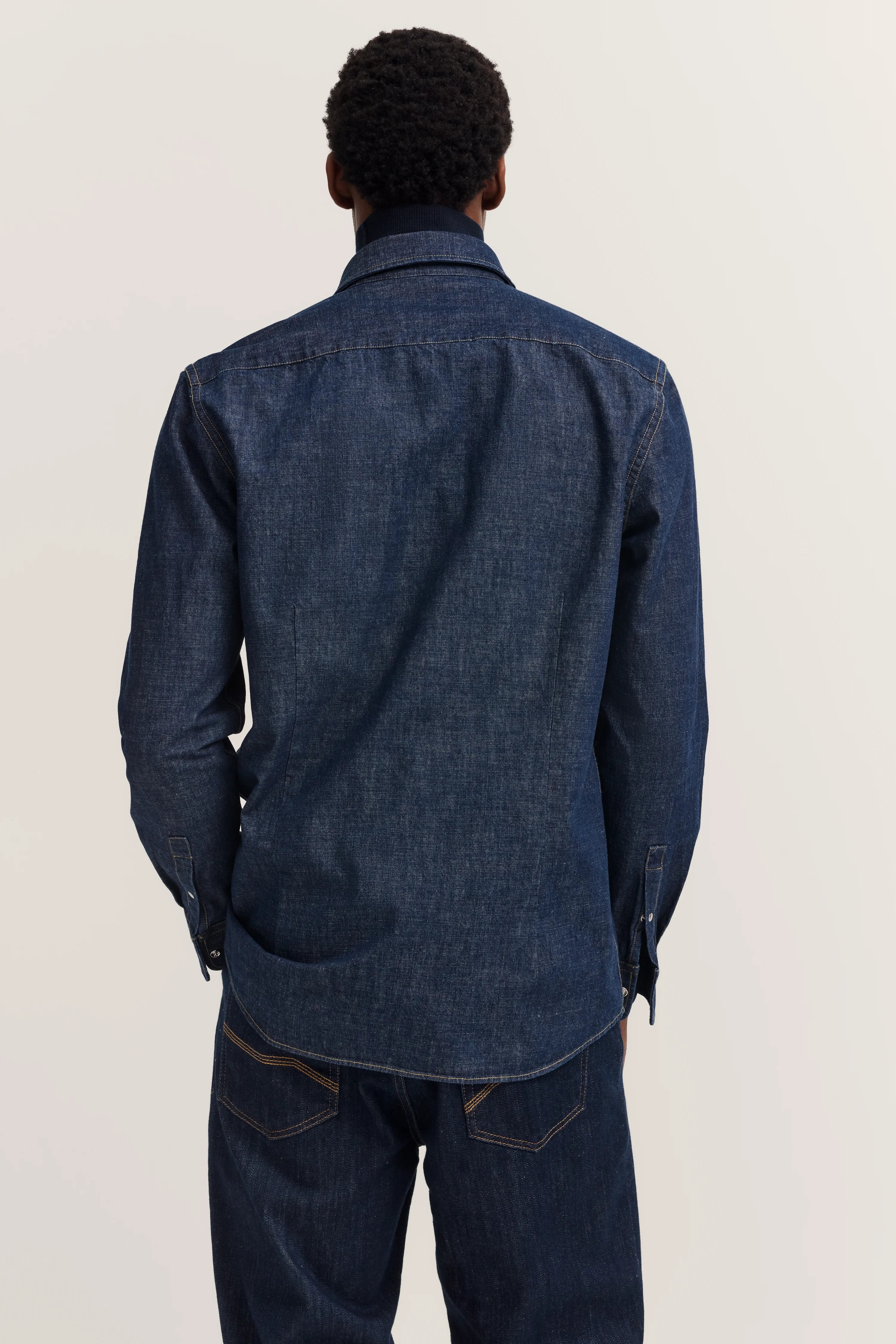 Model in dark denim jacket and jeans, back view, relaxed pose.