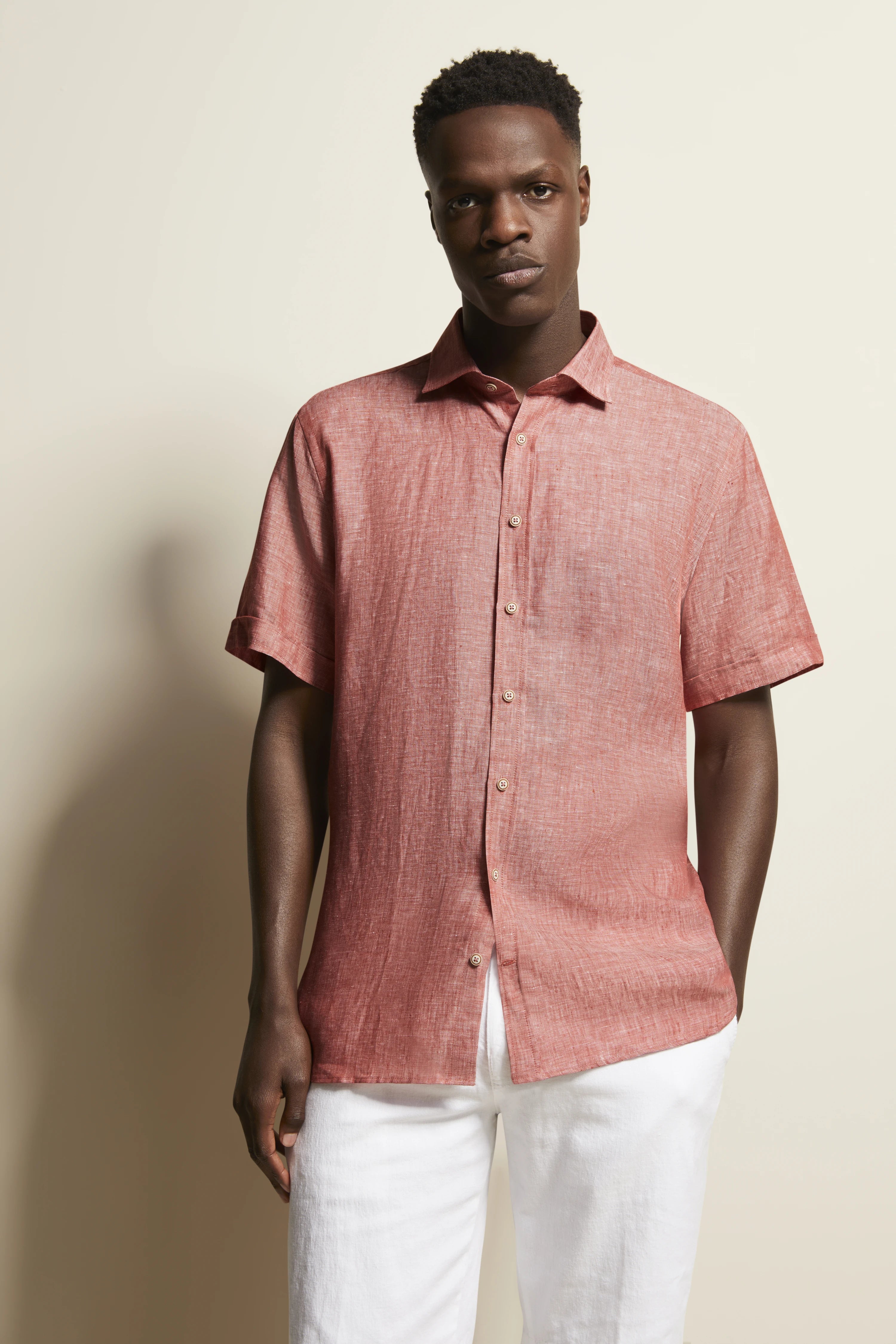 Kurzarm-Hemd in Lachsrot, legeres Modelbild, entspannte Pose, kombiniert mit weißen Hosen.