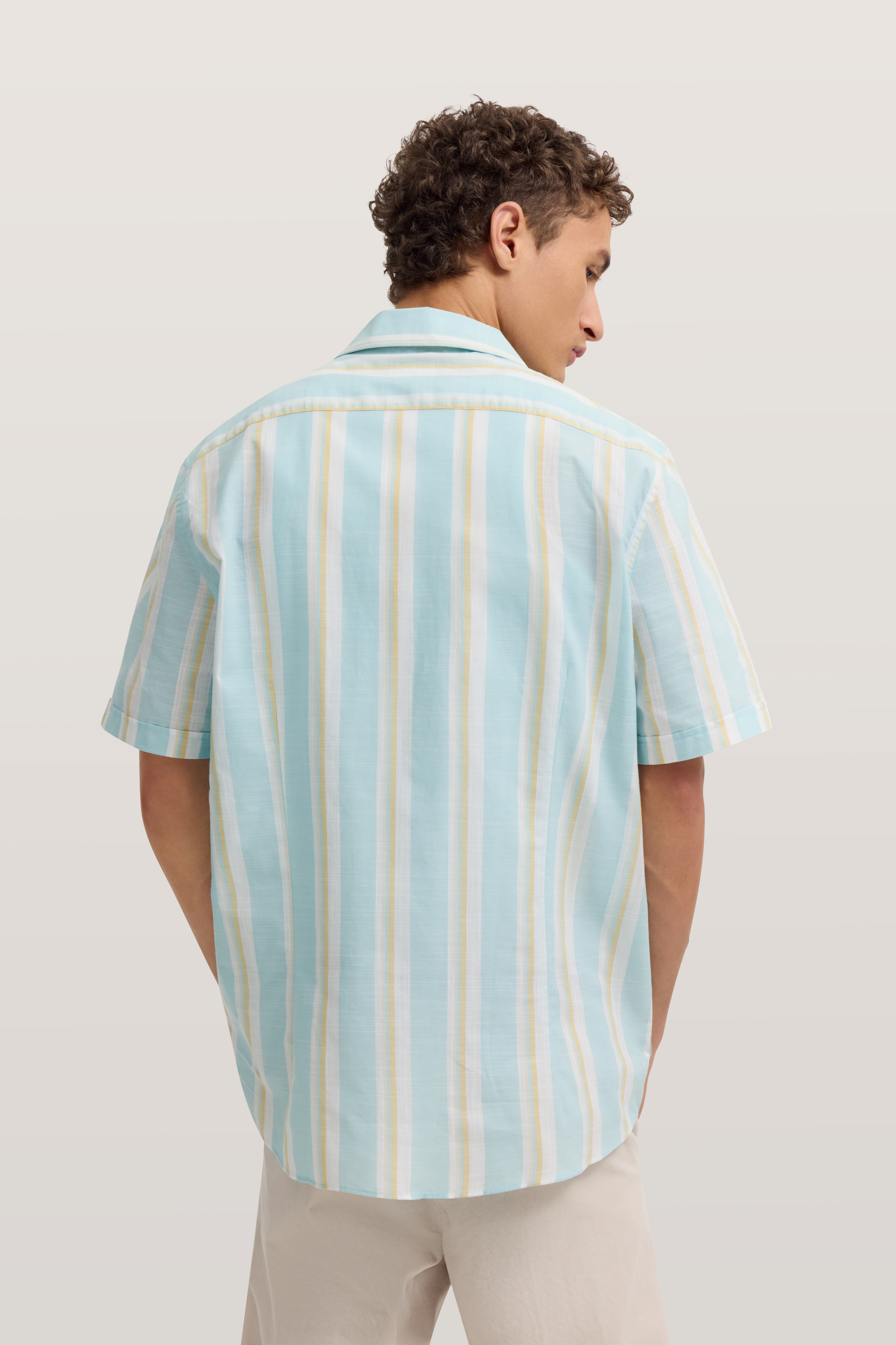 Kurzarmhemd mit blauen und weißen Streifen. Model von hinten. Entspanntes Outfit von bugatti.