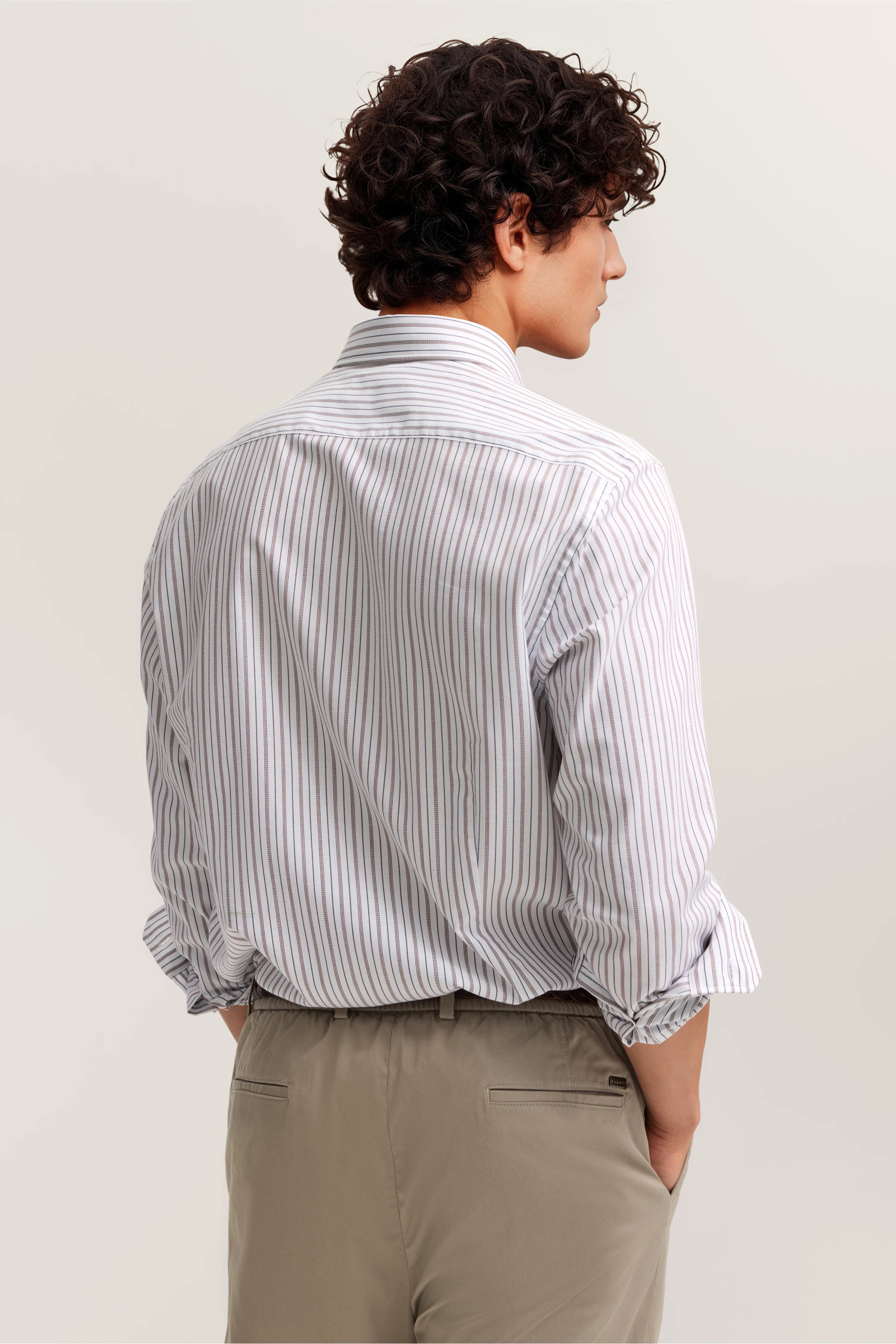 Streifenhemd in Weiß-Blau mit hochgekrempelten Ärmeln, beige Chinohose, Model von hinten.