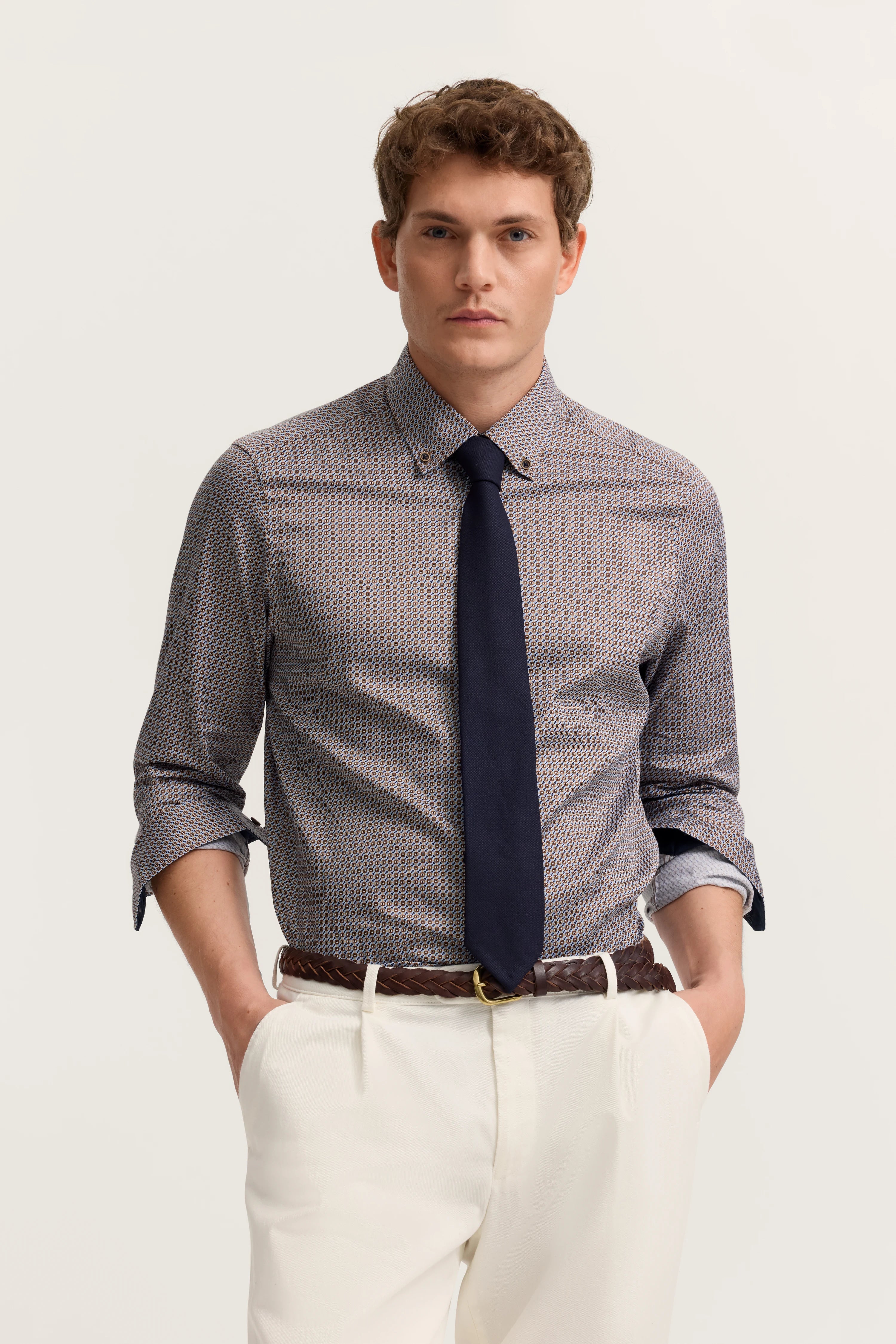 bugatti Modelbild: Mann in gemustertem Hemd, dunkelblauer Krawatte, cremefarbenen Hosen, Hände in Taschen.